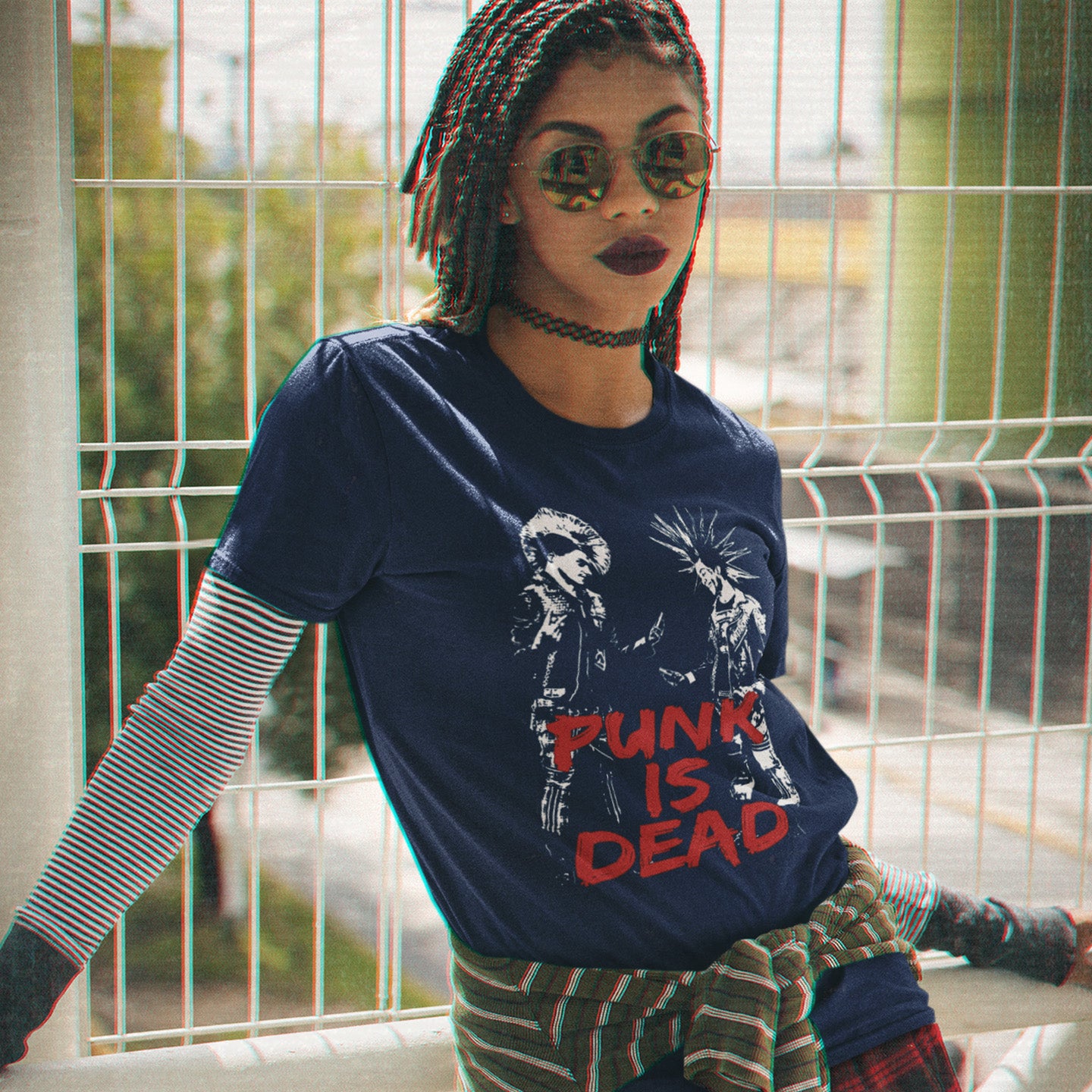 Person wearing a French navy blue t-shirt with 'Punk is Dead' graphic design, sitting on a ledge. A funny punk t shirt suggesting that the mobile phone is a symbol of conformity. This controversial design questions the slogan, 'Punks not dead' by suggesting that reliance on the mobile phone is very unpunk. Made from 100% organic ring-spun cotton, this urban art t shirt is unisex, high-quality, super comfy, and best of all, eco-friendly.