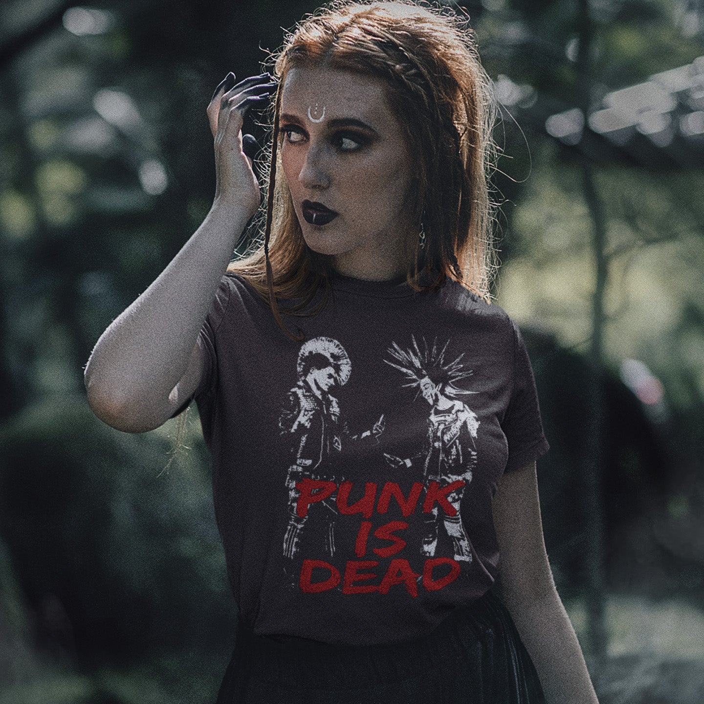 Person wearing a t-shirt with 'Punk is Dead' text and graphic design outdoors. A funny punk t shirt suggesting that the mobile phone is a symbol of conformity. This controversial design questions the slogan, 'Punks not dead' by suggesting that reliance on the mobile phone is very unpunk. Made from 100% organic ring-spun cotton, this urban art t shirt is unisex, high-quality, super comfy, and best of all, eco-friendly.