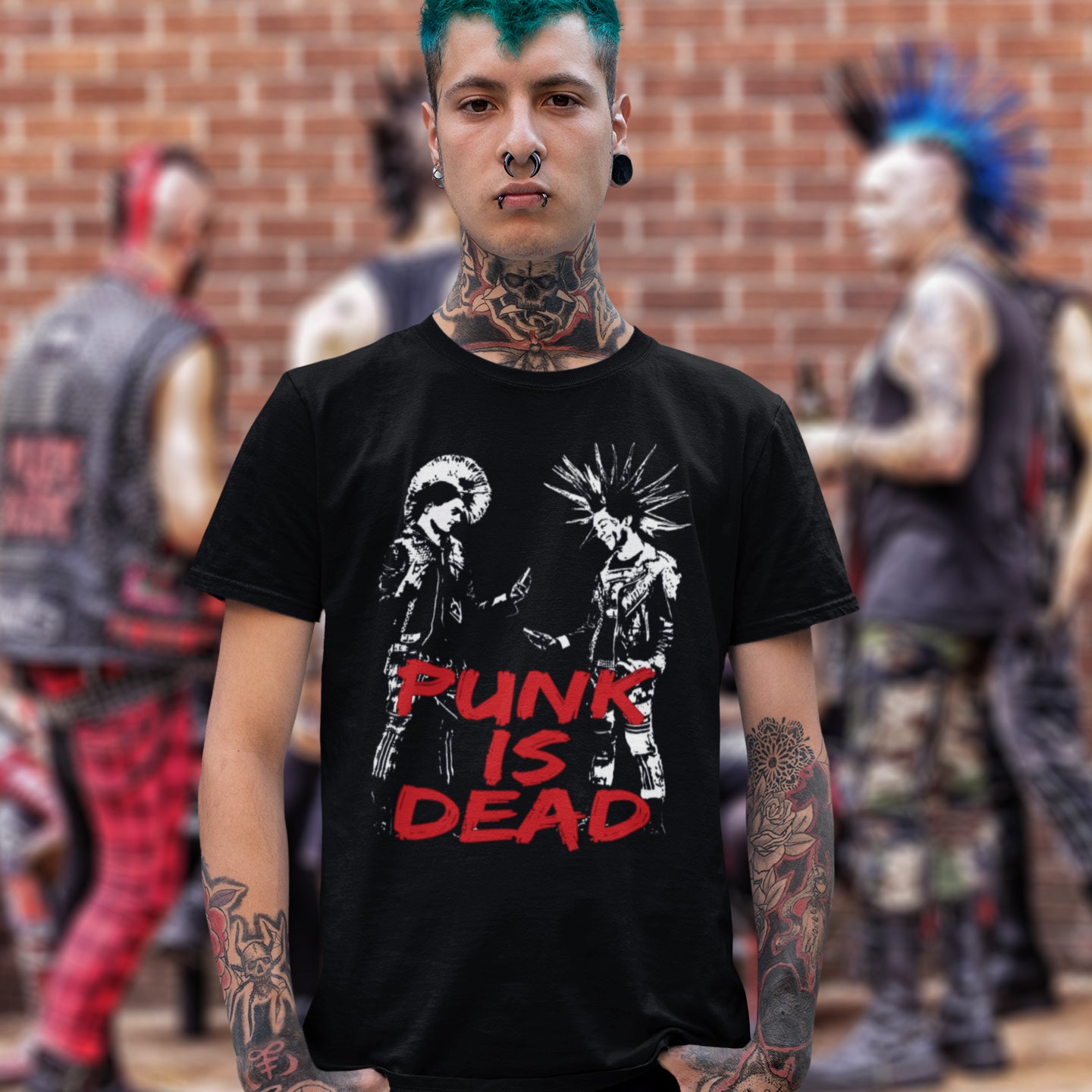 Person wearing a black t-shirt with 'Punk is Dead' graphic and tattoos, standing in front of a brick wall with blurred figures. A funny punk t shirt suggesting that the mobile phone is a symbol of conformity. This controversial design questions the slogan, 'Punks not dead' by suggesting that reliance on the mobile phone is very unpunk. Made from 100% organic ring-spun cotton, this urban art t shirt is unisex, high-quality, super comfy, and best of all, eco-friendly.