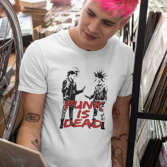 A person with bright pink hair wearing a white graphic t-shirt in a record store setting. The t-shirt features a black graphic of two punk figures and the text 'PUNK IS DEAD' in red.