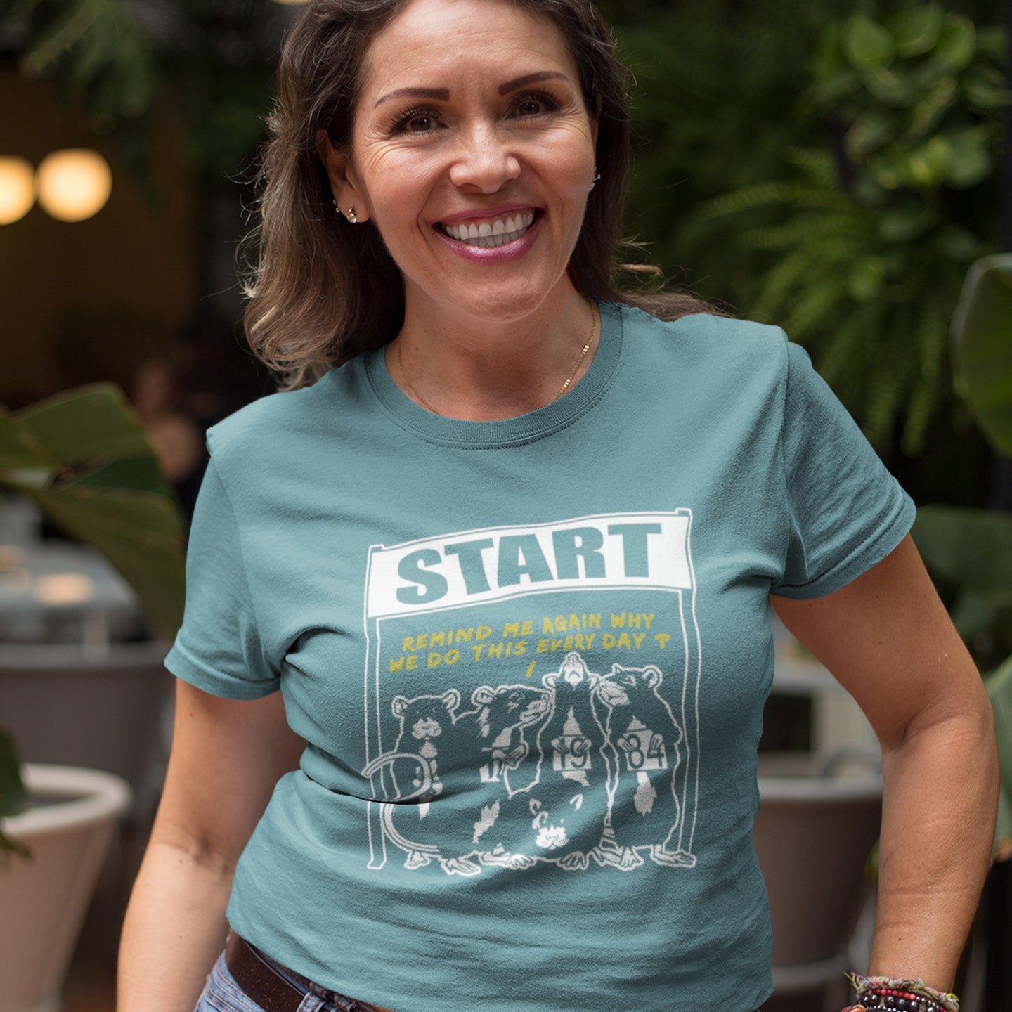 Woman wearing a stargazer t-shirt with a graphic design and text. This Banksy style stencil art t-shirt represents the monotony of everyday working life. A unique satirical design for those times when life starts to feel a little repetitive, unnecessary, and questionable. Made from 100% organic ring-spun cotton, this street art graffiti t-shirt is unisex, high-quality, super comfy, and best of all, eco-friendly.