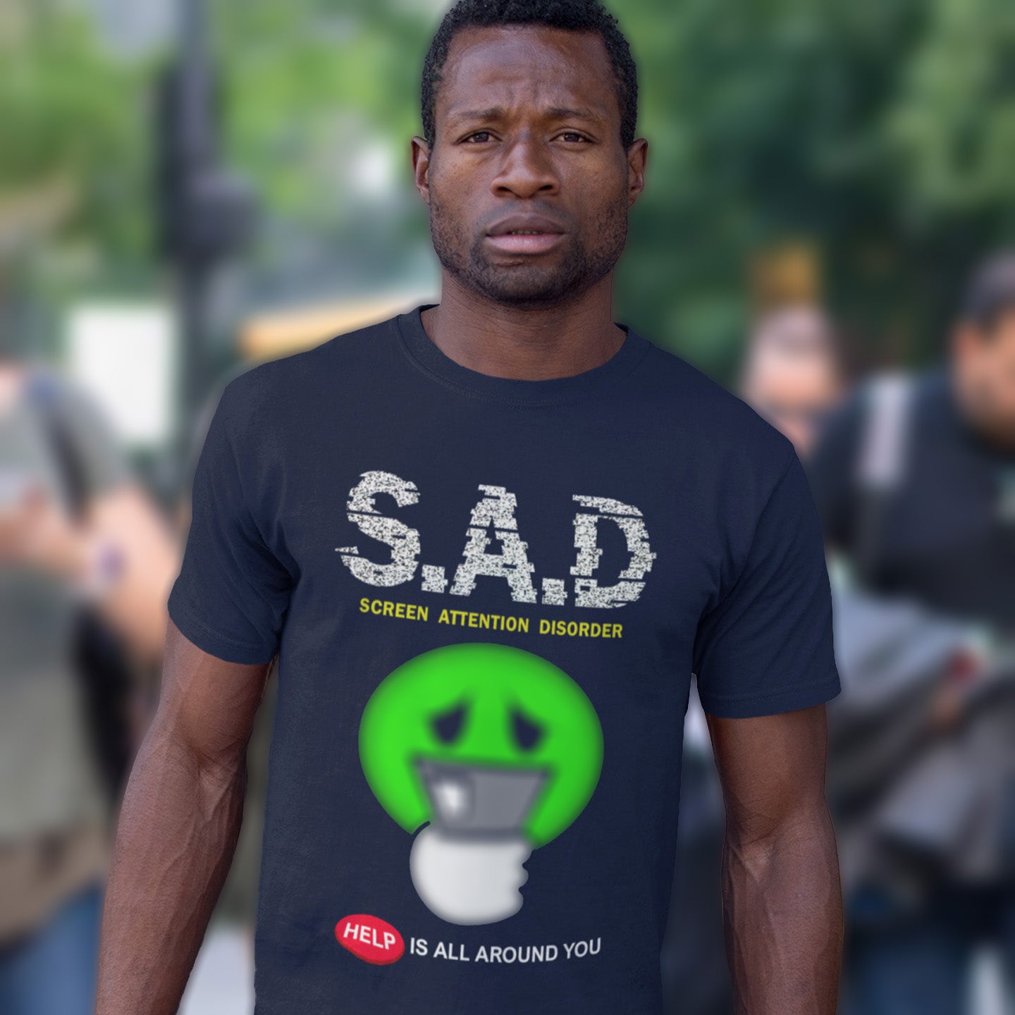 Man wearing a t-shirt with 'S.A.D' and 'Screen Attention Disorder' text, standing outdoors. A funny anti-mobile phone t-shirt. The next time a mobile zombie bumps into you in an empty street don't get angry, show some sympathy and support by wearing this social awareness design. Made from 100% organic ring-spun cotton, this satirical and sarcastic t-shirt is unisex, high-quality, super comfy, and best of all, eco-friendly.