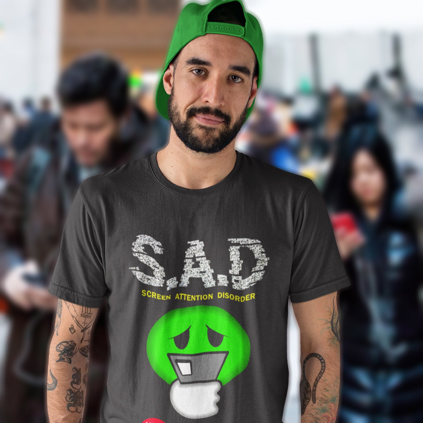 Man wearing a anthracite t-shirt with a green graphic and text, standing in a crowd. A funny anti-mobile phone t-shirt. The next time a mobile zombie bumps into you in an empty street don't get angry, show some sympathy and support by wearing this social awareness design. Made from 100% organic ring-spun cotton, this satirical and sarcastic t-shirt is unisex, high-quality, super comfy, and best of all, eco-friendly.