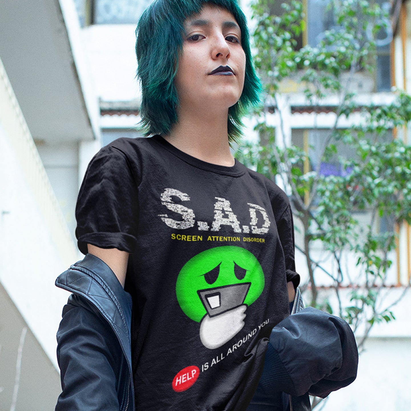 Person wearing a black t-shirt with a graphic design and text, standing outdoors. A funny anti-mobile phone t-shirt. The next time a mobile zombie bumps into you in an empty street don't get angry, show some sympathy and support by wearing this social awareness design. Made from 100% organic ring-spun cotton, this satirical and sarcastic t-shirt is unisex, high-quality, super comfy, and best of all, eco-friendly.