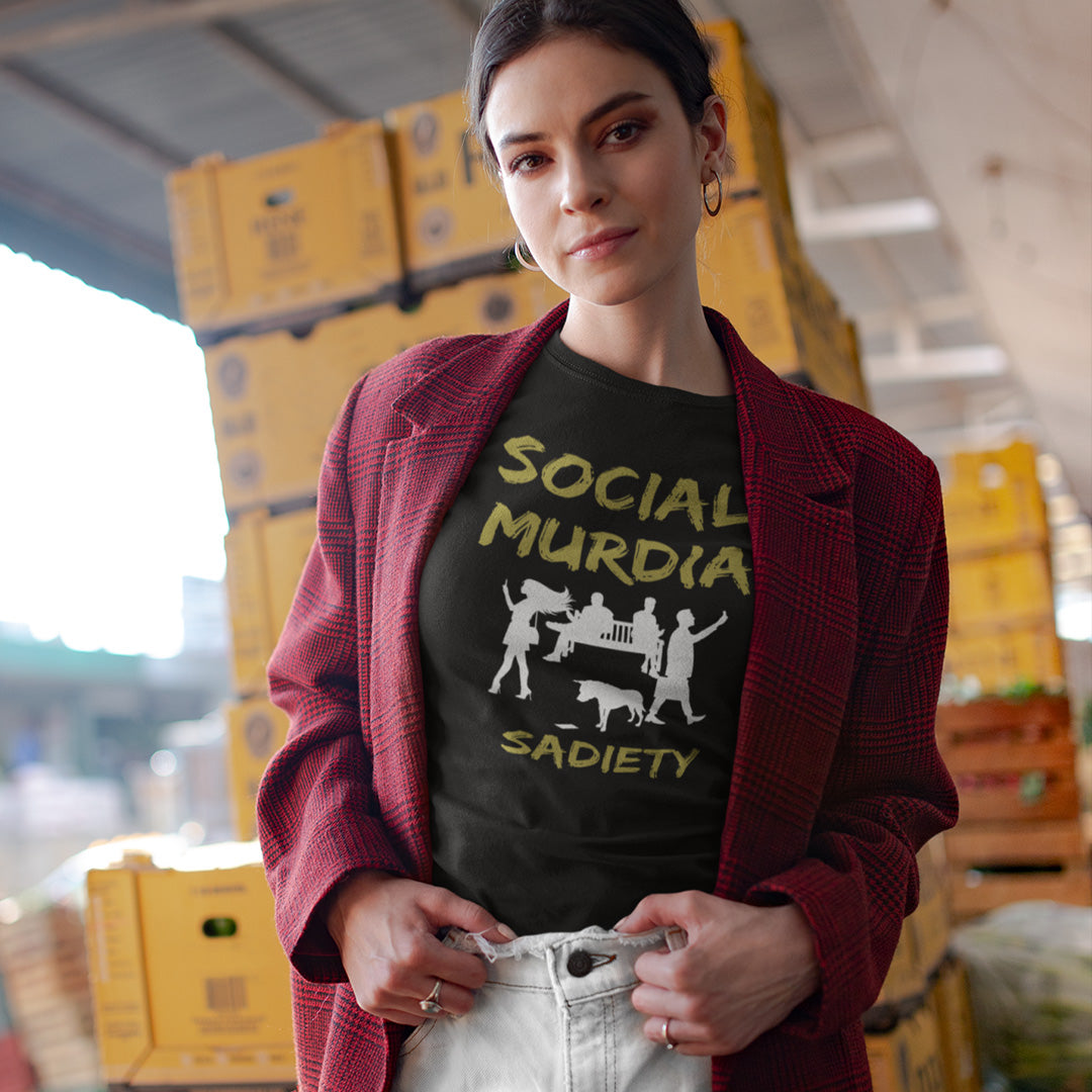 A woman wearing a black graphic t-shirt with a graphic print on the front. The print features the words 'SOCIAL MURDIA' in a textured gold font, a white silhouette of a group of people on smartphones and a dog, and the word 'SADIETY' in the same gold font below.