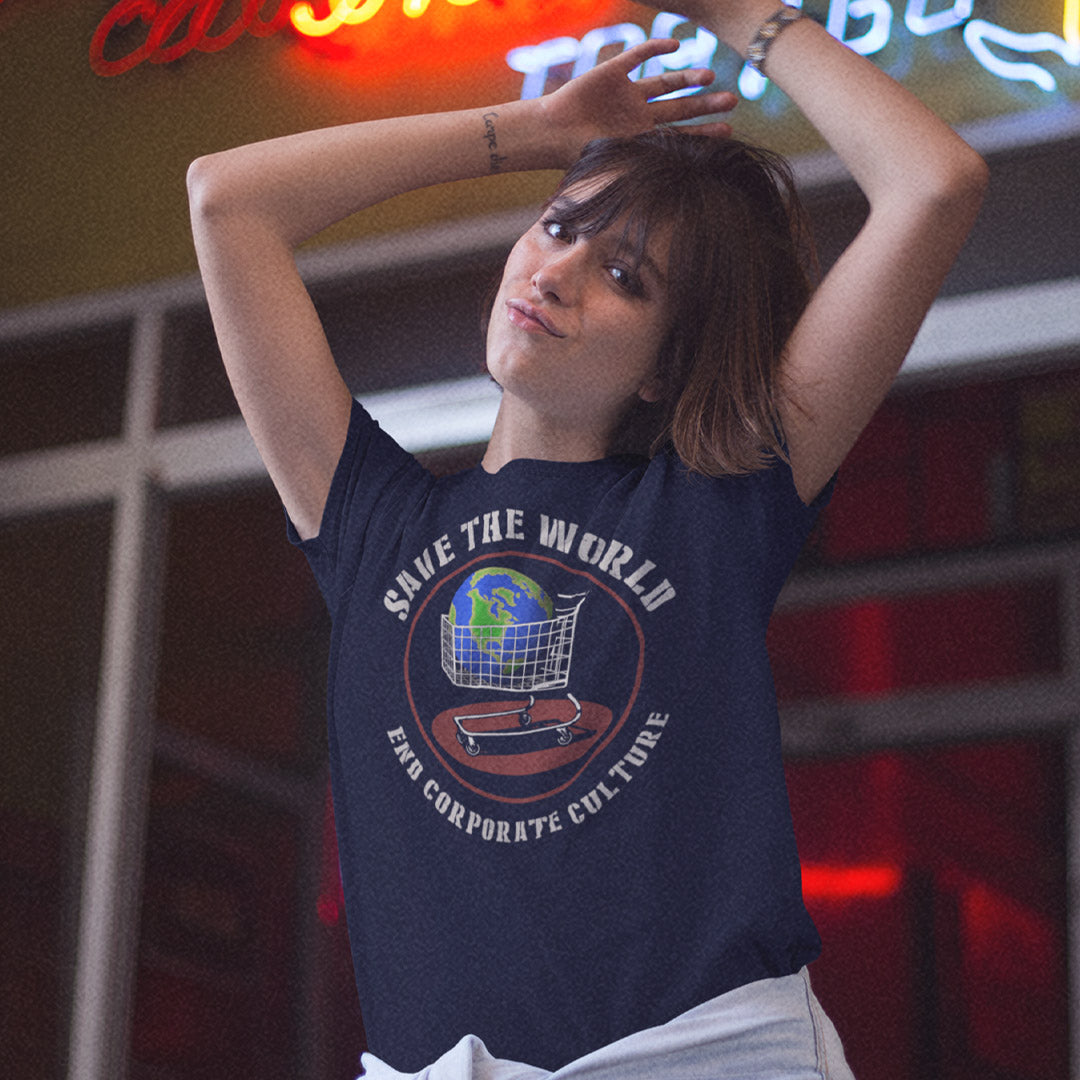 A woman with her arms raised wears a navy blue graphic t-shirt featuring a globe and shopping cart design with the text 'SAVE THE WORLD' and 'END CORPORATE CULTURE'. The background shows a dimly lit, neon-lit environment.
