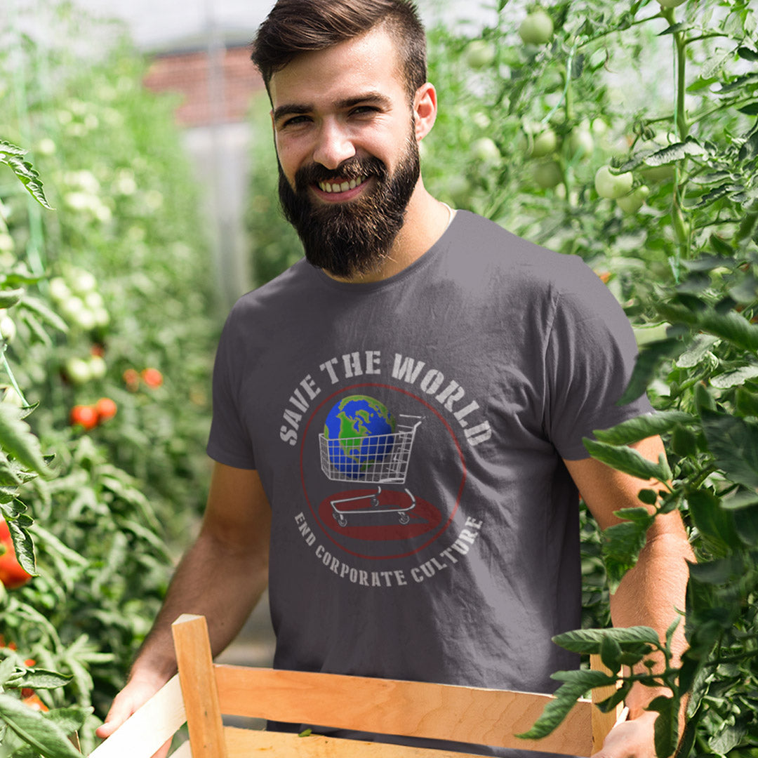 A smiling bearded man wearing a dark gray graphic t-shirt stands in a tomato garden holding a wooden crate. The t-shirt features a graphic with a shopping cart and globe, surrounded by the text 'SAVE THE WORLD' and 'END CORPORATE CULTURE'.