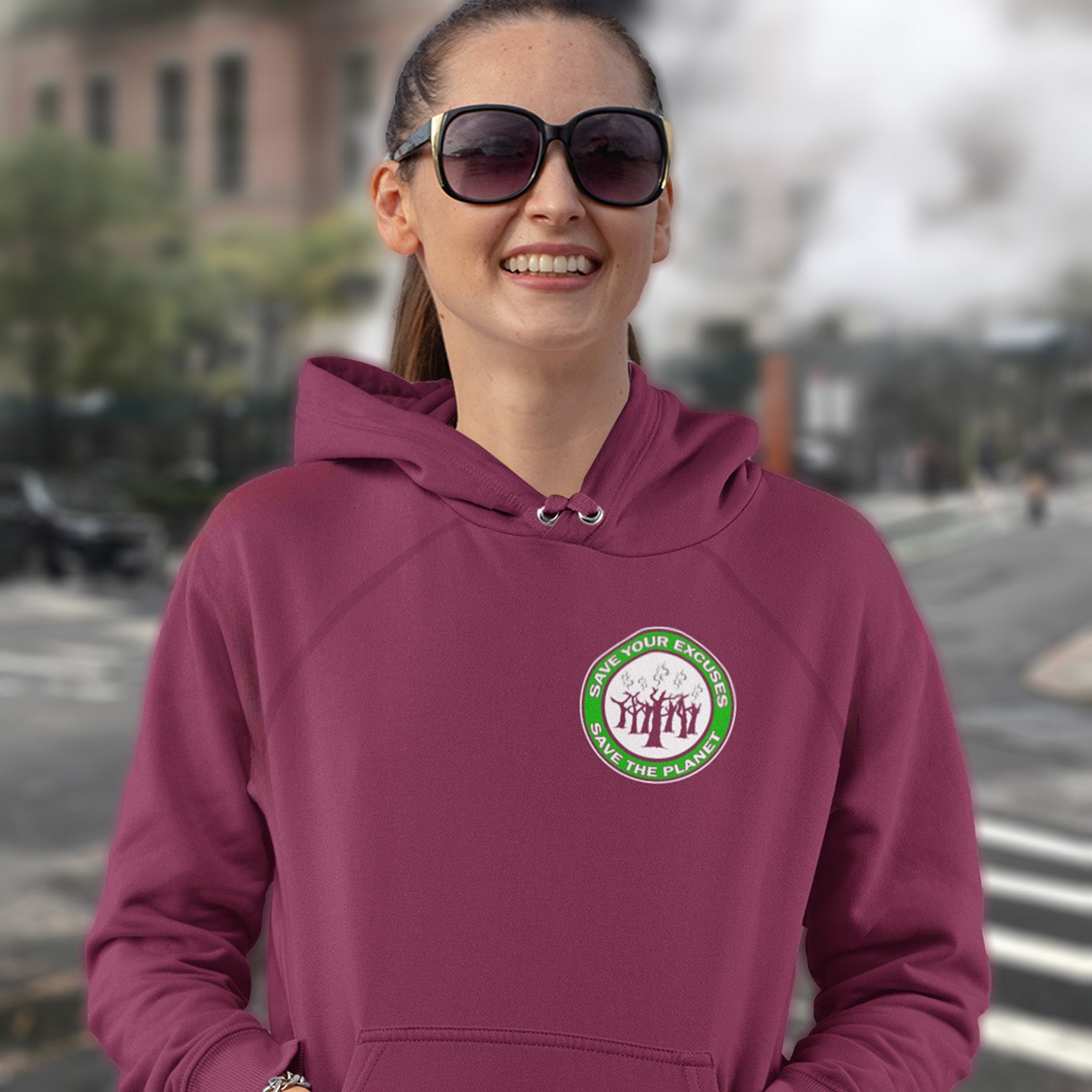 Person wearing a burgundy hoodie with a logo on a street background. A save the planet t-shirt that promotes social awareness of environmental issues. It's time to stop making poor excuses for why we haven't got around to saving our planet yet. Comfortable and practical. It's extra soft and has a convenient front pouch pocket. Made from organic cotton and recycled polyester, this environmental awareness hoodie is a great eco-friendly choice.