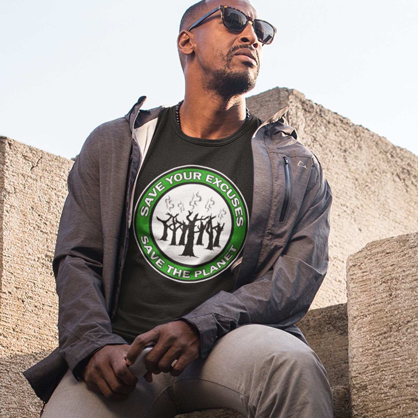 Man wearing a t-shirt with a green and white graphic and text, sitting outdoors. A 'save the planet' t-shirt that promotes social awareness of environmental issues. It's time to stop making poor excuses for why our governments haven't got around to saving our planet yet. Made from 100% organic ring-spun cotton, this environmental awareness t-shirt is unisex, high-quality, super comfy, and best of all, eco-friendly.