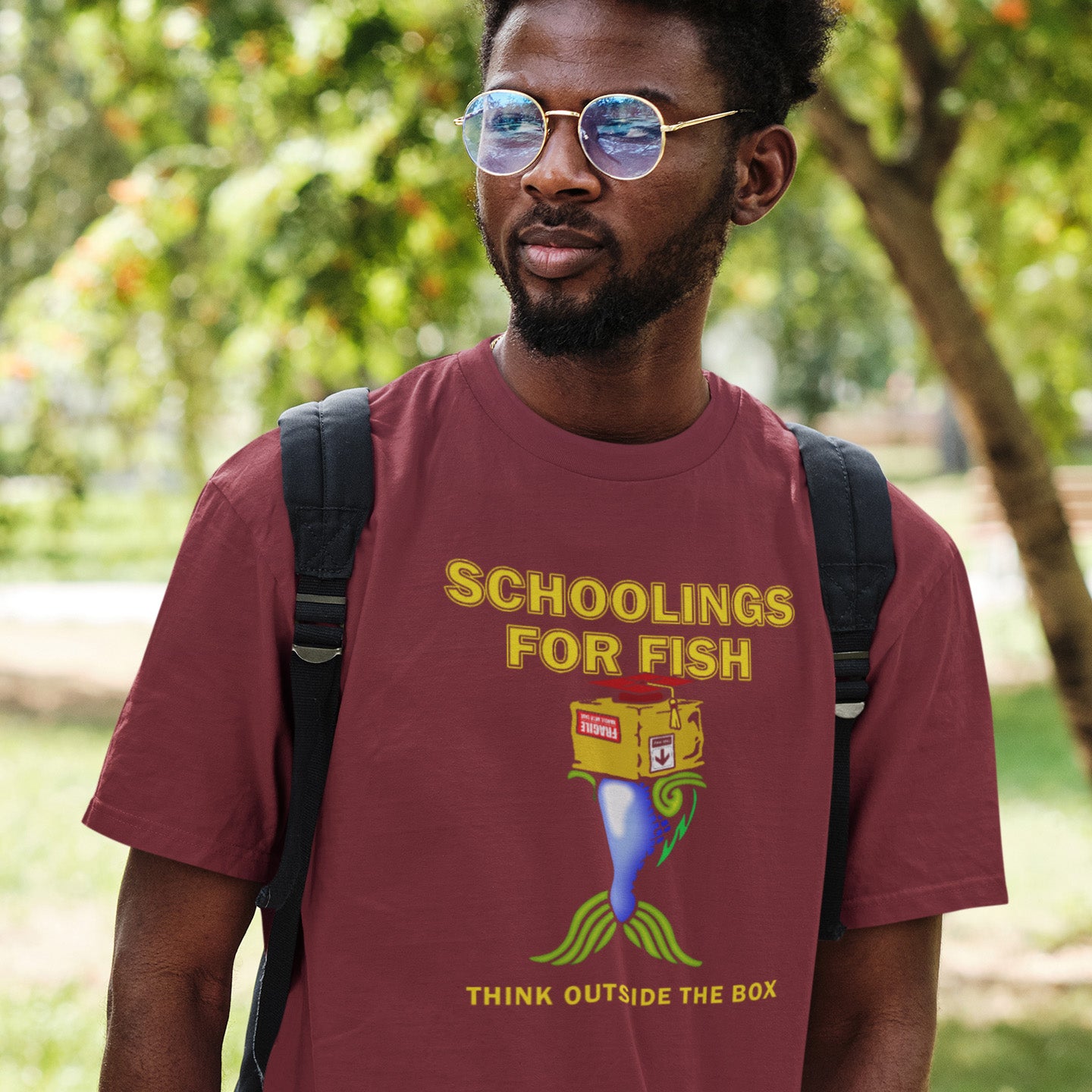 Man wearing a burgundy t-shirt with a graphic design and text, standing outdoors. This alternative education non conformist t shirt design conveys a feeling that we are not quite being taught the full picture by our educational system. Great choice for any disgruntled student. Made from 100% organic ring-spun cotton, this witty counter culture t shirt is unisex, high-quality, super comfy, and best of all, eco-friendly.