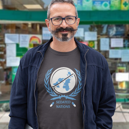 Man wearing a t-shirt with a graphic design and text, standing in front of a store with various items on display. This anti drugs t shirt suggests an overuse of pharmaceutical drugs in the developed world. Are we united or just overly sedated ? A very satirical view questioning the effects of capitalism on the health care pharmaceutical industry. Made from 100% organic ring-spun cotton, this counter culture t shirt is unisex, high quality, super comfy, and best of all, eco-friendly.
