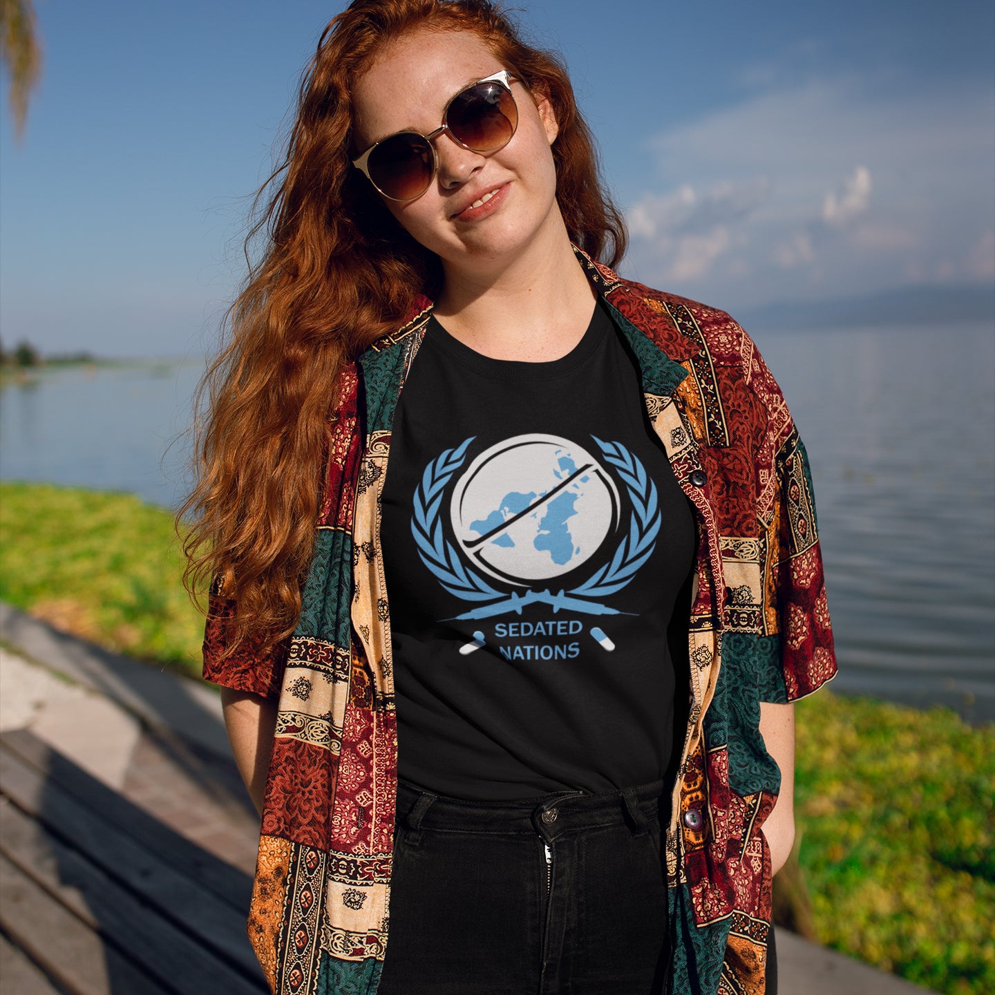 Woman wearing a black t shirt with 'sedated nations' logo, standing near a lake. This anti drugs t shirt suggests an overuse of pharmaceutical drugs in the developed world. Are we united or just overly sedated ? A very satirical view questioning the effects of capitalism on the health care pharmaceutical industry. Made from 100% organic ring-spun cotton, this counter culture t shirt is unisex, high quality, super comfy, and best of all, eco-friendly.