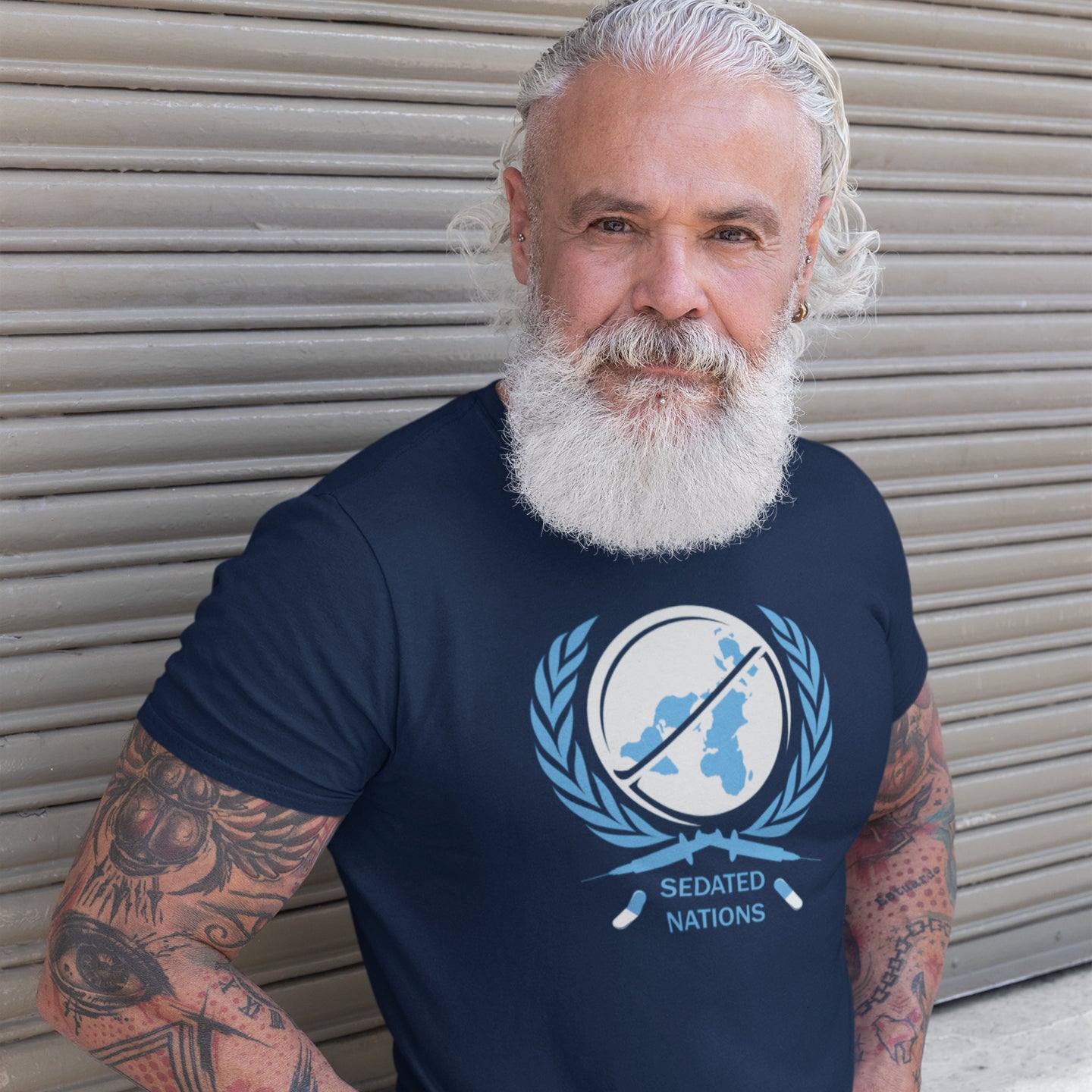 Man wearing a French navy blue t-shirt with a logo and text, standing against a metallic shutter. This anti drugs t shirt suggests an overuse of pharmaceutical drugs in the developed world. Are we united or just overly sedated ? A very satirical view questioning the effects of capitalism on the health care pharmaceutical industry. Made from 100% organic ring-spun cotton, this counter culture t shirt is unisex, high quality, super comfy, and best of all, eco-friendly.