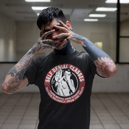 Person wearing a black t-shirt with a graphic design and text, covering their face with their hands. This emotional intelligence t shirt satirically highlights self denial as an increasing part of everyday life and suggests we could provide classes to improve it. This sarcastic urban art design laughs at people who want to protect themselves from the truth. Made from 100% organic ring-spun cotton, this broken society t shirt is unisex, high-quality, super comfy, and best of all, eco-friendly.