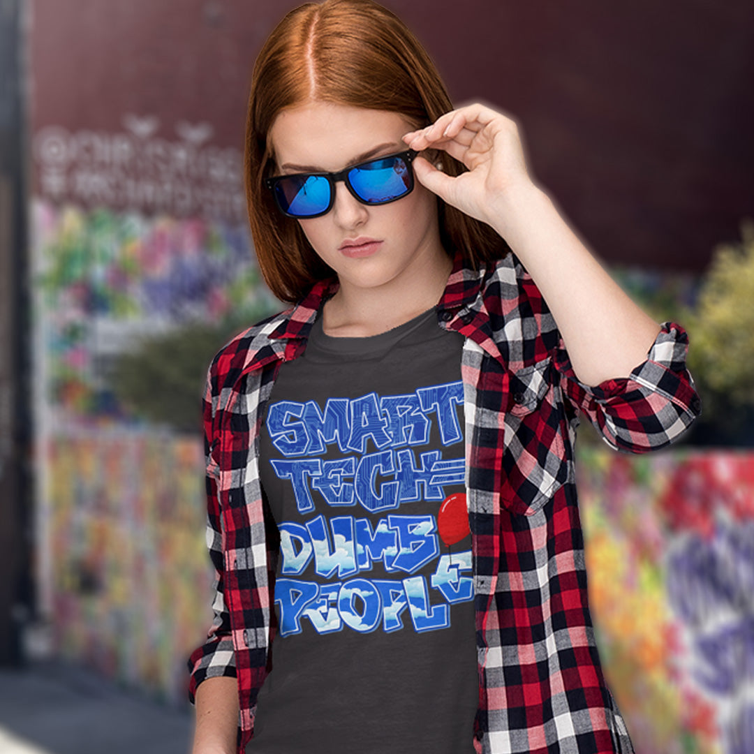 Person wearing a shirt with 'Smart Tech Dumbs People' text and plaid jacket, outdoors. This anti ai t shirt design suggests that the smarter the technology gets the dumber the people become. This contemporary design is ideal if you like t shirts for intellectuals and would rather exercise your mind than rely on machinery to do your thinking for you. Made from 100% organic ring-spun cotton, this non conformist t shirt is unisex, high-quality, super comfy, and best of all, eco-friendly.