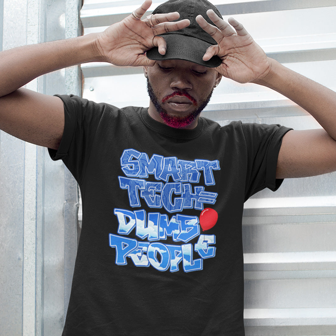 Person wearing a black t-shirt with blue and red text, standing indoors. This anti ai t shirt design suggests that the smarter the technology gets the dumber the people become. This contemporary design is ideal if you like t shirts for intellectuals and would rather exercise your mind than rely on machinery to do your thinking for you. Made from 100% organic ring-spun cotton, this non conformist t shirt is unisex, high-quality, super comfy, and best of all, eco-friendly.