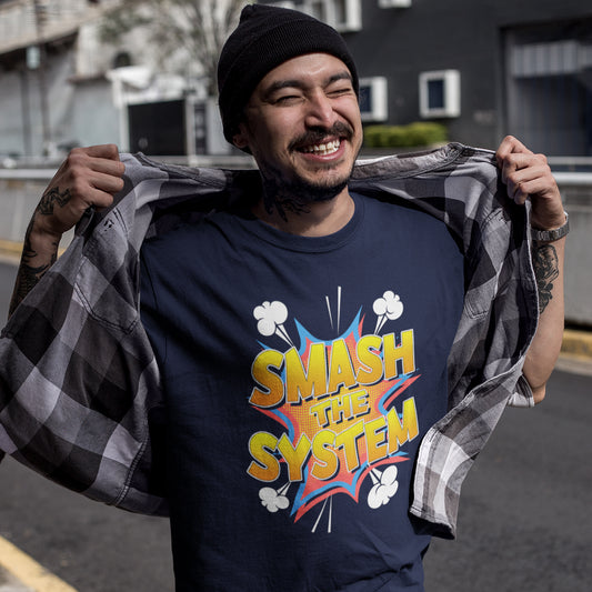 A man wearing a navy blue graphic t-shirt with a colorful 'SMASH THE SYSTEM' comic-style print, holding open a black and white plaid flannel shirt over his shoulders. He is wearing a black beanie and has visible tattoos on his arms, set against an outdoor street background.