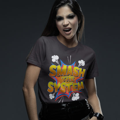A woman wearing a dark gray graphic t-shirt with a colorful comic-style 'SMASH THE SYSTEM' print, paired with black pants, against a dark gray studio background.