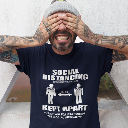 Man wearing a French navy blue t-shirt with a humorous social distancing message, standing against a light-coloured wall. An anti government t shirt design representing a much older form of social distancing in our society. Class inequality. This anti establishment t-shirt design promote social awareness of the class divide our system creates. Made from 100% organic ring-spun cotton, this non conformist t shirt is unisex, high-quality, super comfy, and best of all, eco-friendly.