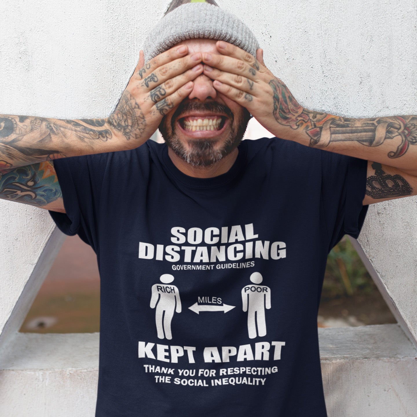 Man wearing a French navy blue t-shirt with a humorous social distancing message, standing against a light-coloured wall. A class war t-shirt design representing a much older form of social distancing in our society. Class inequality. This anti-establishment t-shirt design promote social awareness of the class divide our system creates. Made from 100% organic ring-spun cotton, this nonconformist t-shirt is unisex, high-quality, super comfy, and best of all, eco-friendly.