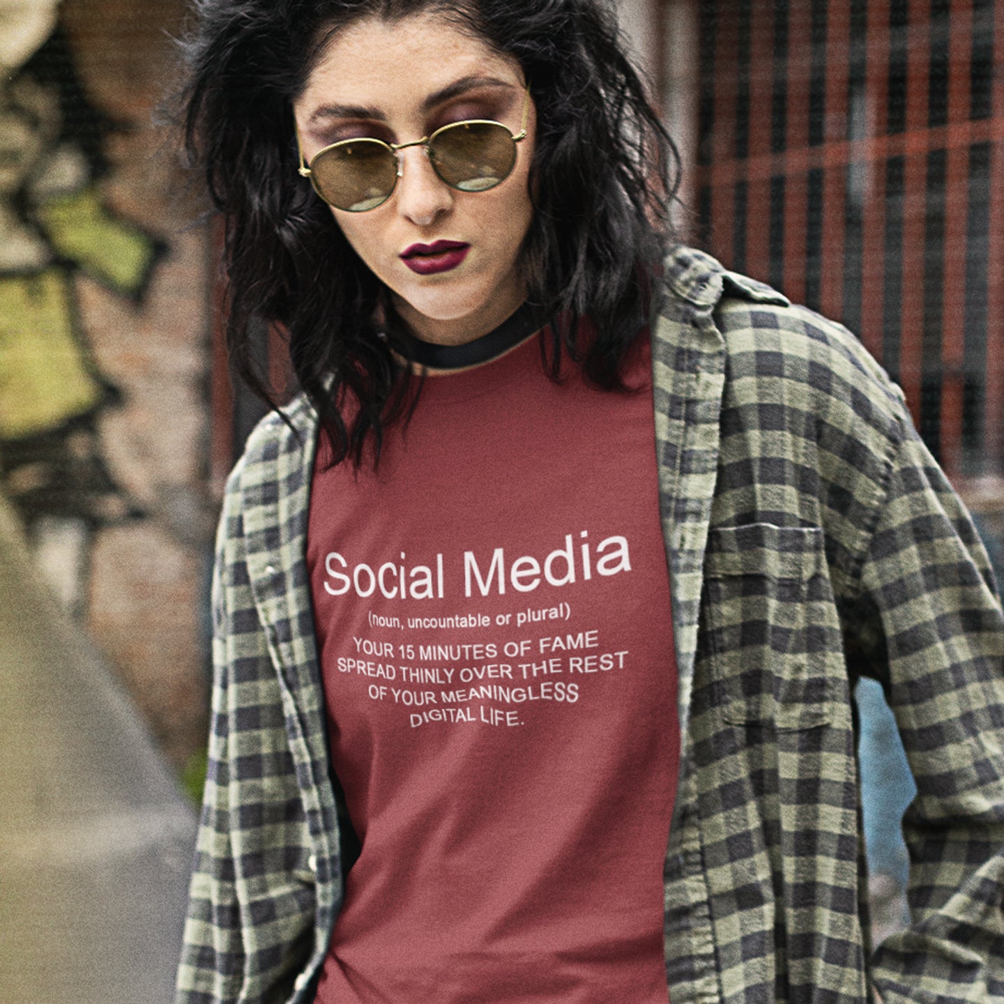Person wearing a burgundy t-shirt with 'Social Media' text, standing against a graffiti-covered wall. An anti-social media t-shirt with a humorous definition. A unique t-shirt design for those who still have a real life and consider 'community' to be something you can touch and walk around. Made from 100% organic ring-spun cotton, this anti social media t-shirt is unisex, high-quality, super comfy, and best of all, eco-friendly.