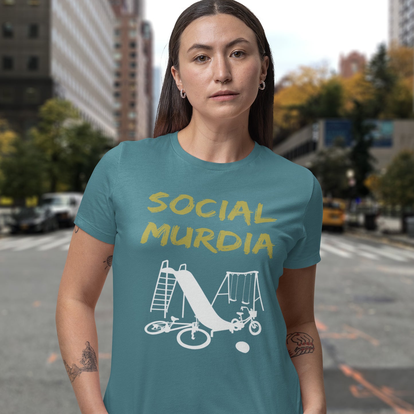 Person wearing a stargazer t-shirt with 'SOCIAL MURDIA' text and graphic on a city street background. This counterculture t-shirt promoting social awareness of the effect of social media on our children. A unique design depicting how social media is probably murdering our society and leaving our playgrounds empty. Made from 100% organic ring-spun cotton, this anti-mobile phone t-shirt is unisex, high-quality, super comfy, and best of all, eco-friendly.