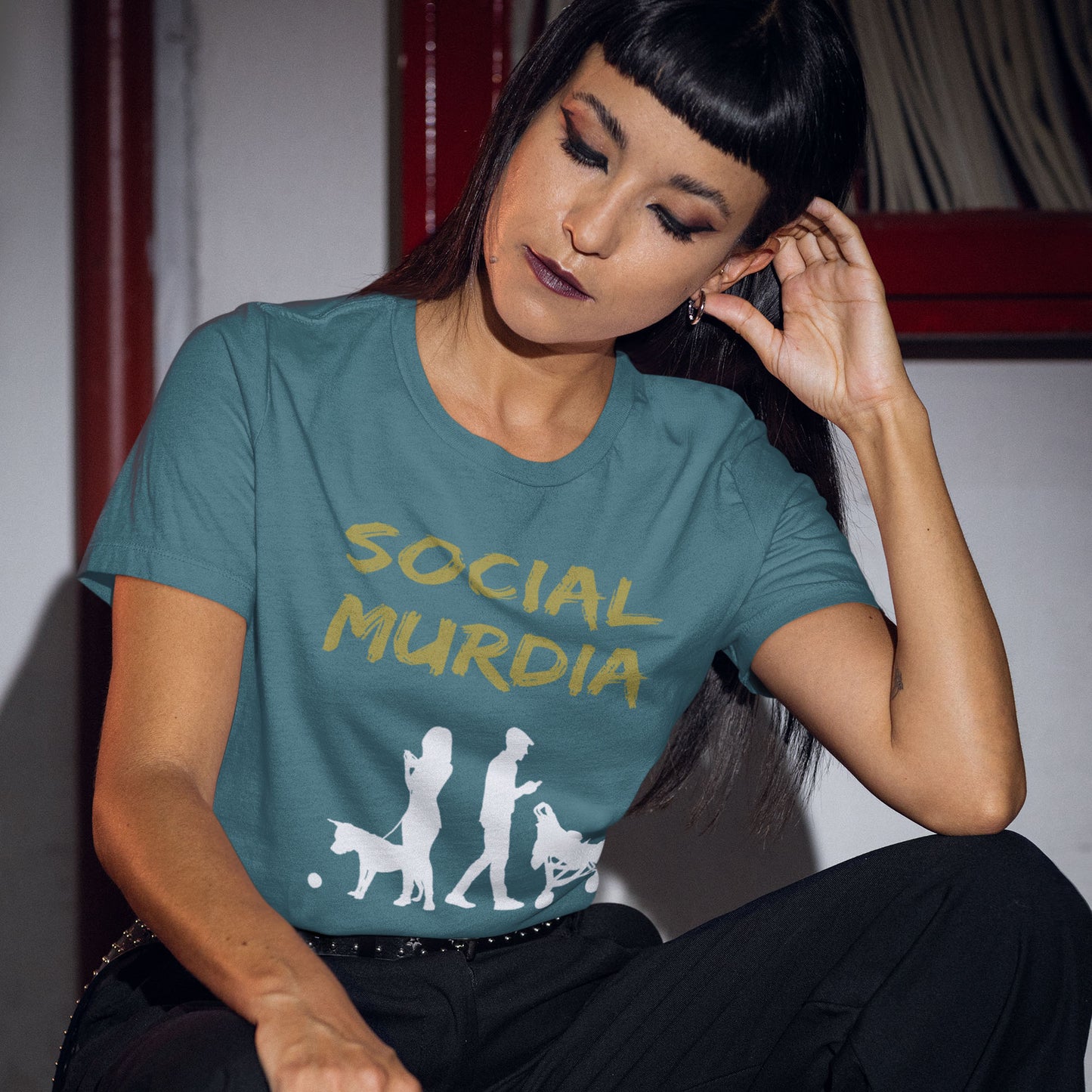 Woman wearing a teal t-shirt with 'SOCIAL MURDIA' text and graphic. An anti-social media t-shirt arguing against the abuse of social media and mobile phones. The main aim of social media is to connect people, but it doesn't look like that from street level. This anti-mobile phone design suggests society is actually being murdered by media on mobiles. Made from 100% organic ring-spun cotton, this social awareness t-shirt is unisex, high-quality, super comfy, and best of all, eco-friendly.