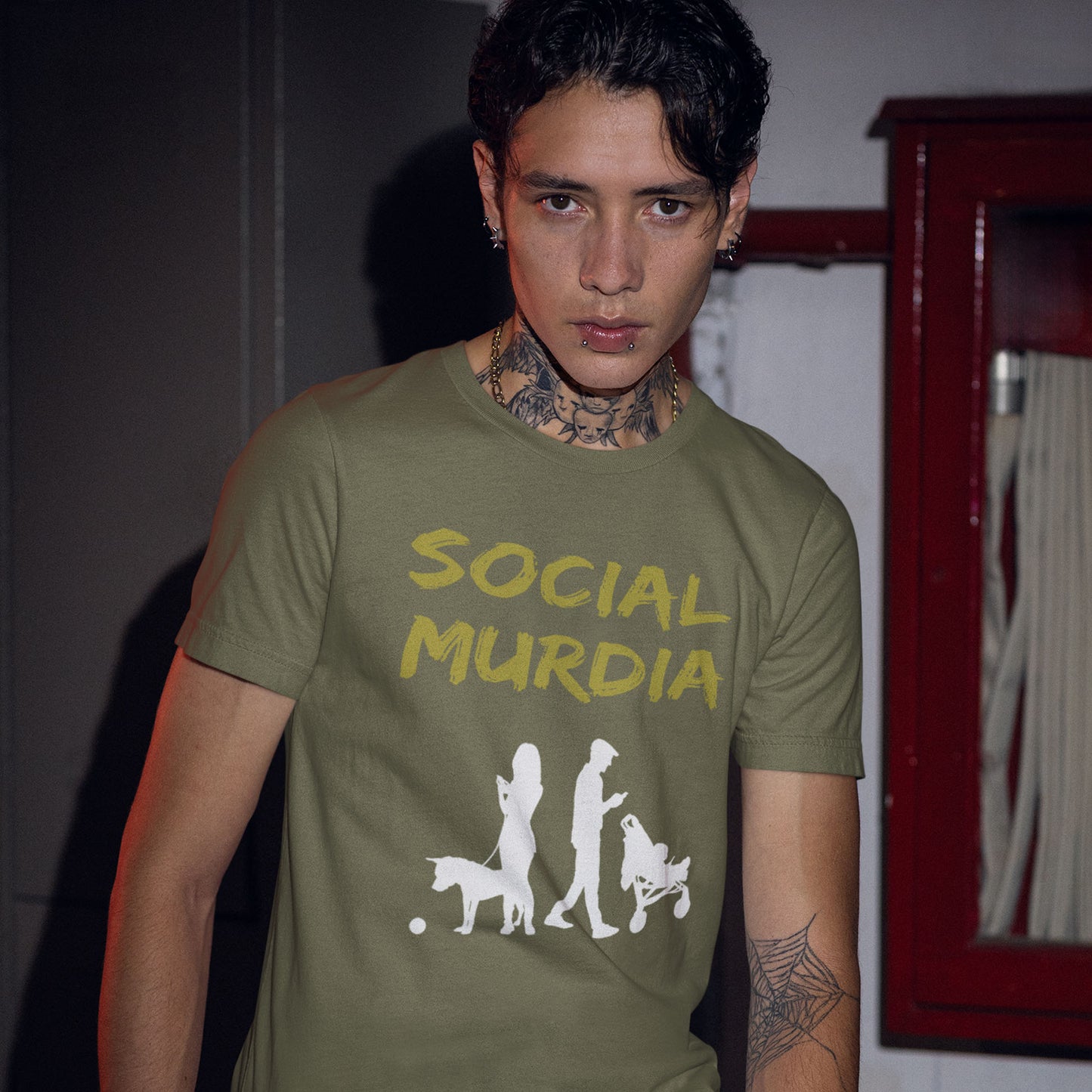 Person wearing a green t-shirt with 'Social Murdia' design indoors. An anti-social media t-shirt arguing against the abuse of social media and mobile phones. The main aim of social media is to connect people, but it doesn't look like that from street level. This anti-mobile phone design suggests society is actually being murdered by media on mobiles. Made from 100% organic ring-spun cotton, this social awareness t-shirt is unisex, high-quality, super comfy, and best of all, eco-friendly.