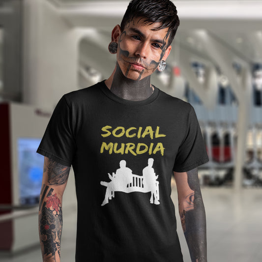 A man with tattoos and face paint wearing a black t-shirt with a yellow and white graphic that reads 'SOCIAL MURDIA' above a white silhouette of two figures sitting on a bench.