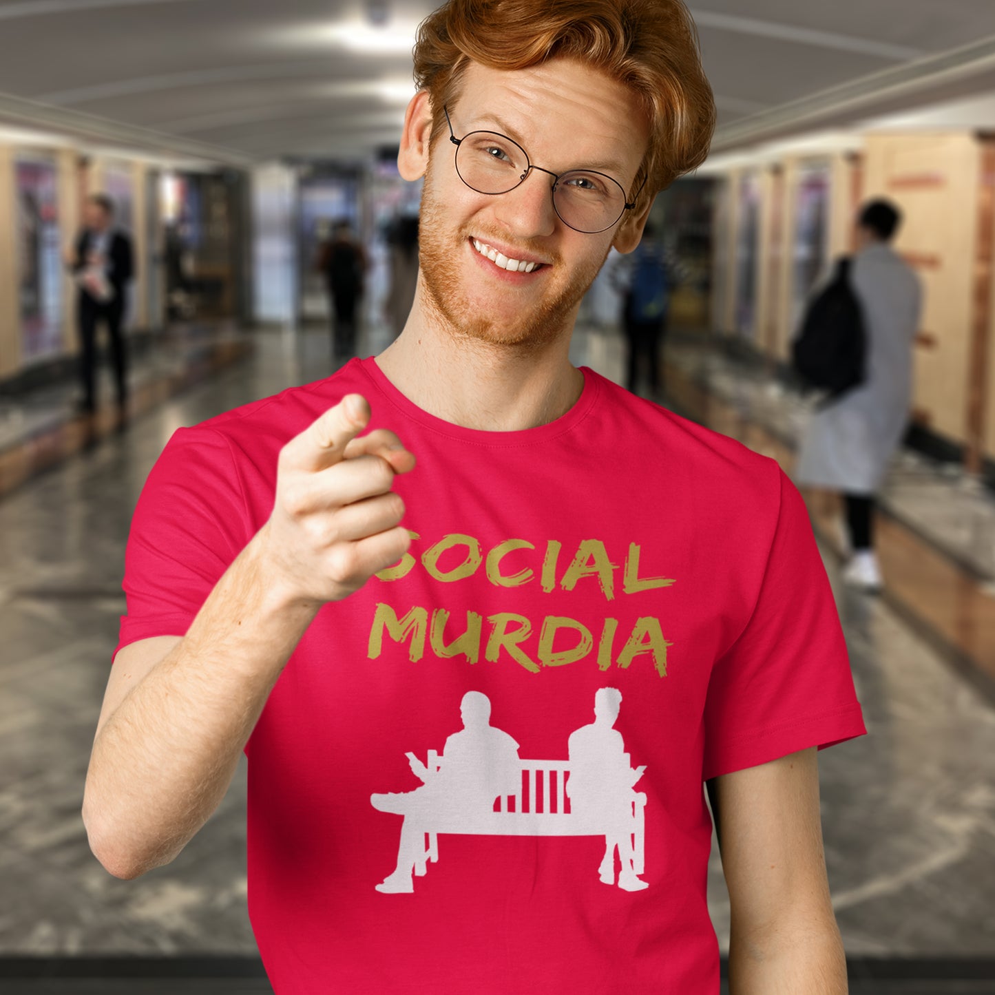 Person wearing a red t-shirt with 'SOCIAL MURDIA' text and graphic in a blurred indoor setting. An anti-social media t-shirt arguing against the abuse of social media and mobile phones.  This anti-mobile phone design suggests society is actually being murdered by media on mobiles. Made from 100% organic ring-spun cotton, this anti-social media t-shirt is unisex, high-quality, super comfy, and best of all, eco-friendly.