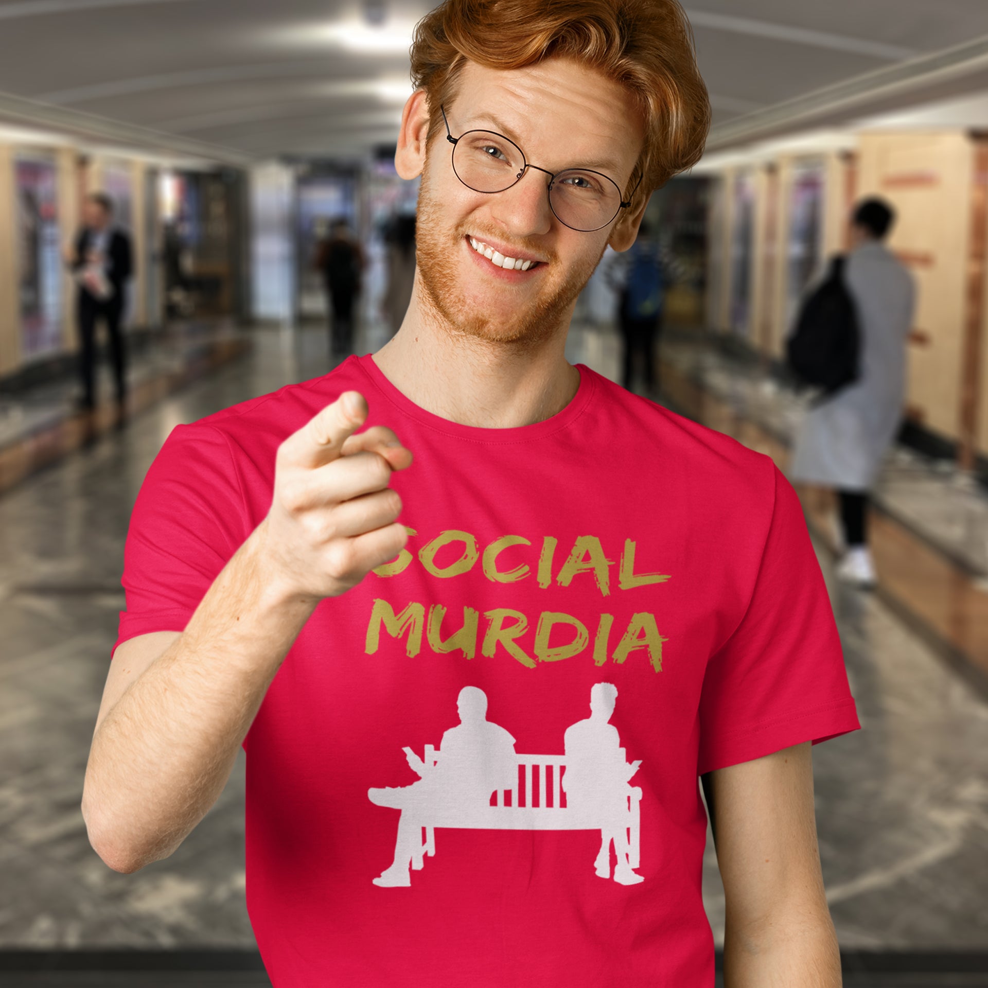 Person wearing a red t-shirt with 'SOCIAL MURDIA' text and graphic in a blurred indoor setting. An anti-social media t-shirt arguing against the abuse of social media and mobile phones.  This anti-mobile phone design suggests society is actually being murdered by media on mobiles. Made from 100% organic ring-spun cotton, this anti-social media t-shirt is unisex, high-quality, super comfy, and best of all, eco-friendly.