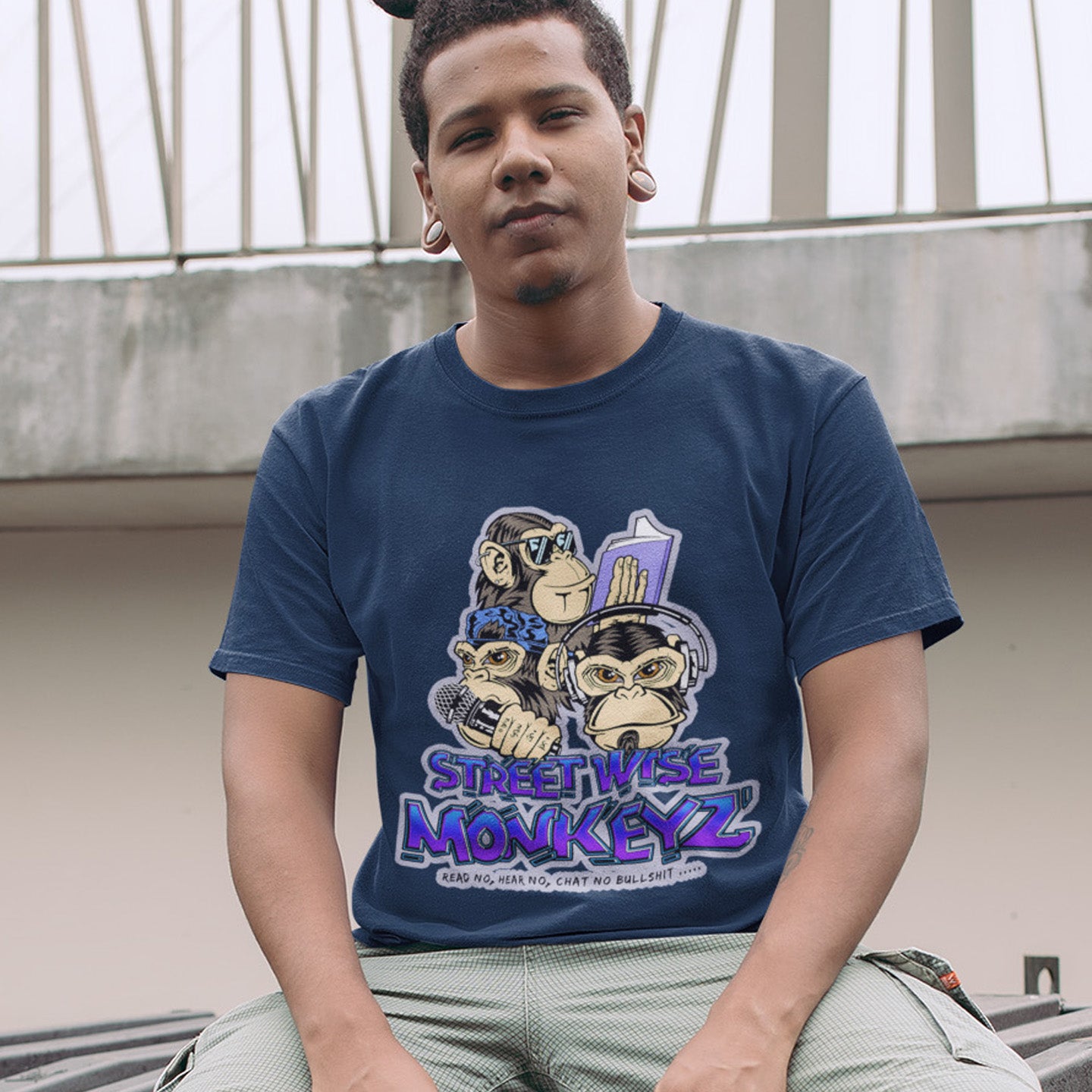 Man in a French navy t-shirt sitting outdoors. A street art graffiti t-shirt design depicting a modern slant on the three wise monkeys. It's time to be street wise. Hear and see everything and have your say. The time for ignorance is over. Made from 100% organic ring-spun cotton, this street art t-shirt is unisex, high-quality, super comfy, and best of all, eco-friendly.