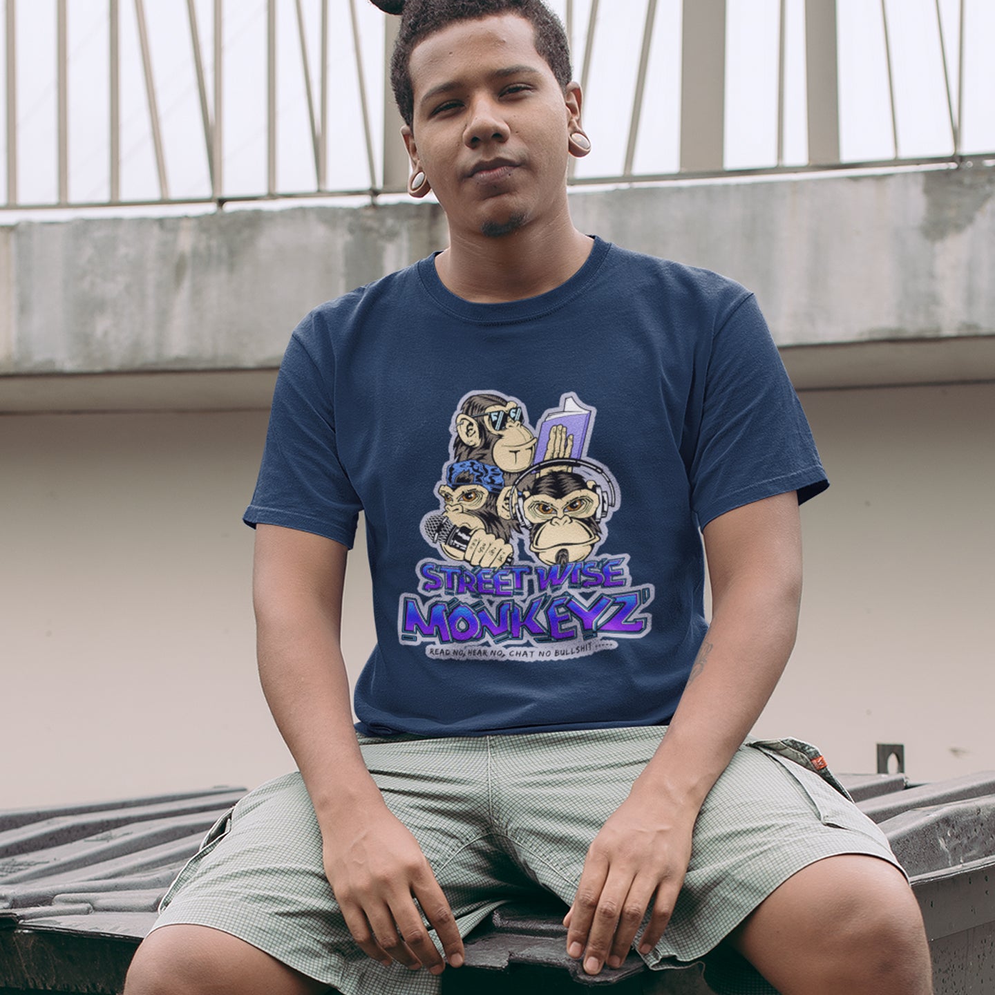 Person wearing a French navy blue t-shirt with 'Streetwise Monkeyz' design, sitting outdoors. A urban graffiti t shirt design depicting a modern slant on the three wise monkeys. It's time to be street wise. Hear and see everything and have your say. The time for ignorance is over. Made from 100% organic ring-spun cotton, this urban art t shirt is unisex, high-quality, super comfy, and best of all, eco-friendly.
