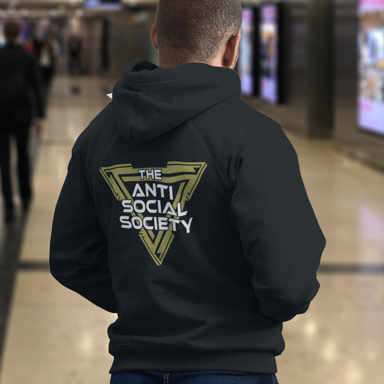 Person wearing a black hoodie with 'The Anti Social Society' logo in a mall. This anti-social hoodie design gives you an oxymoron to ponder, the more and more you don't want to be a member, the more you become one. A satirical counterculture dig at modern society. Comfortable and practical. It's extra soft and has a convenient front pouch pocket. Made from organic cotton and recycled polyester, this social awareness hoodie is a great eco-friendly choice.