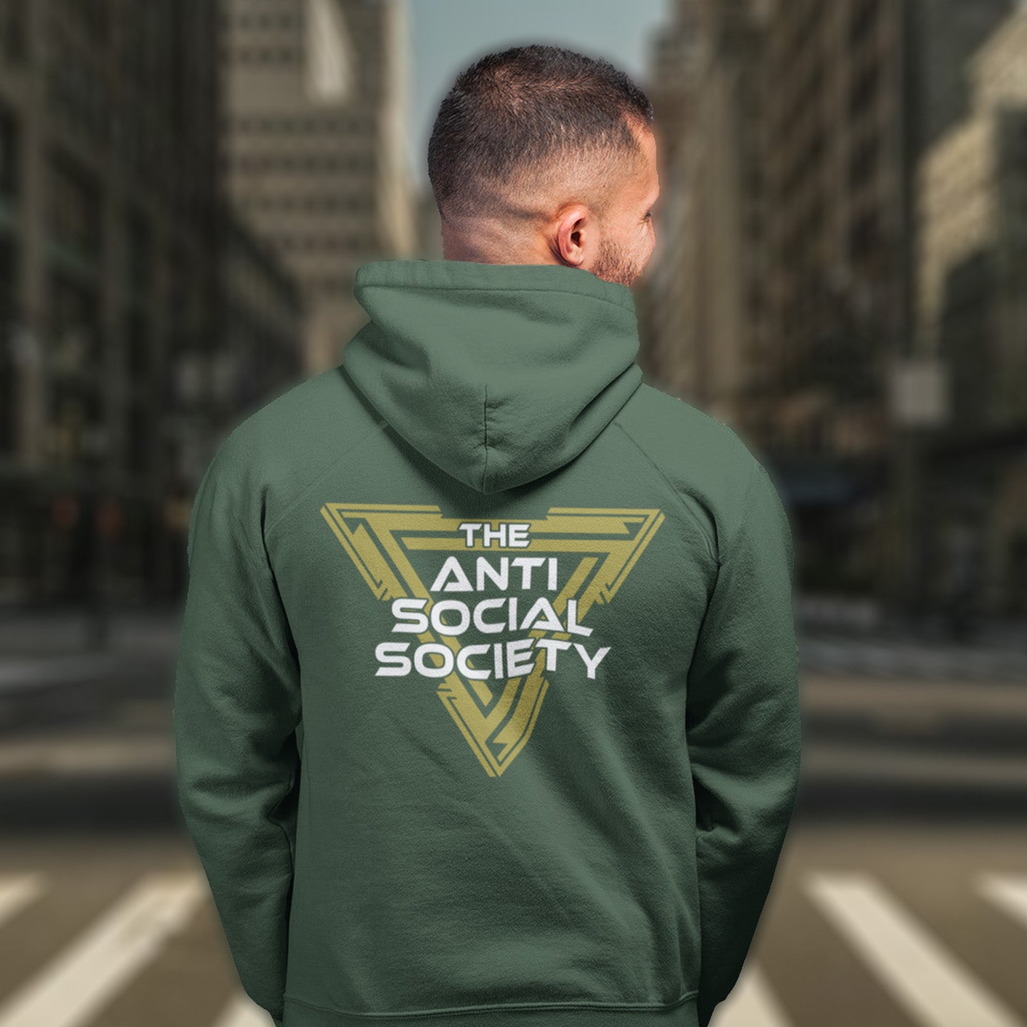 Person wearing a bottle green hoodie with 'The Anti Social Society' logo on the back, standing in an urban setting. This anti-social hoodie design gives you an oxymoron to ponder, the more and more you don't want to be a member, the more you become one. A satirical counterculture dig at modern society. Comfortable and practical. It's extra soft and has a convenient front pouch pocket. Made from organic cotton and recycled polyester, this social awareness hoodie is a great eco-friendly choice.