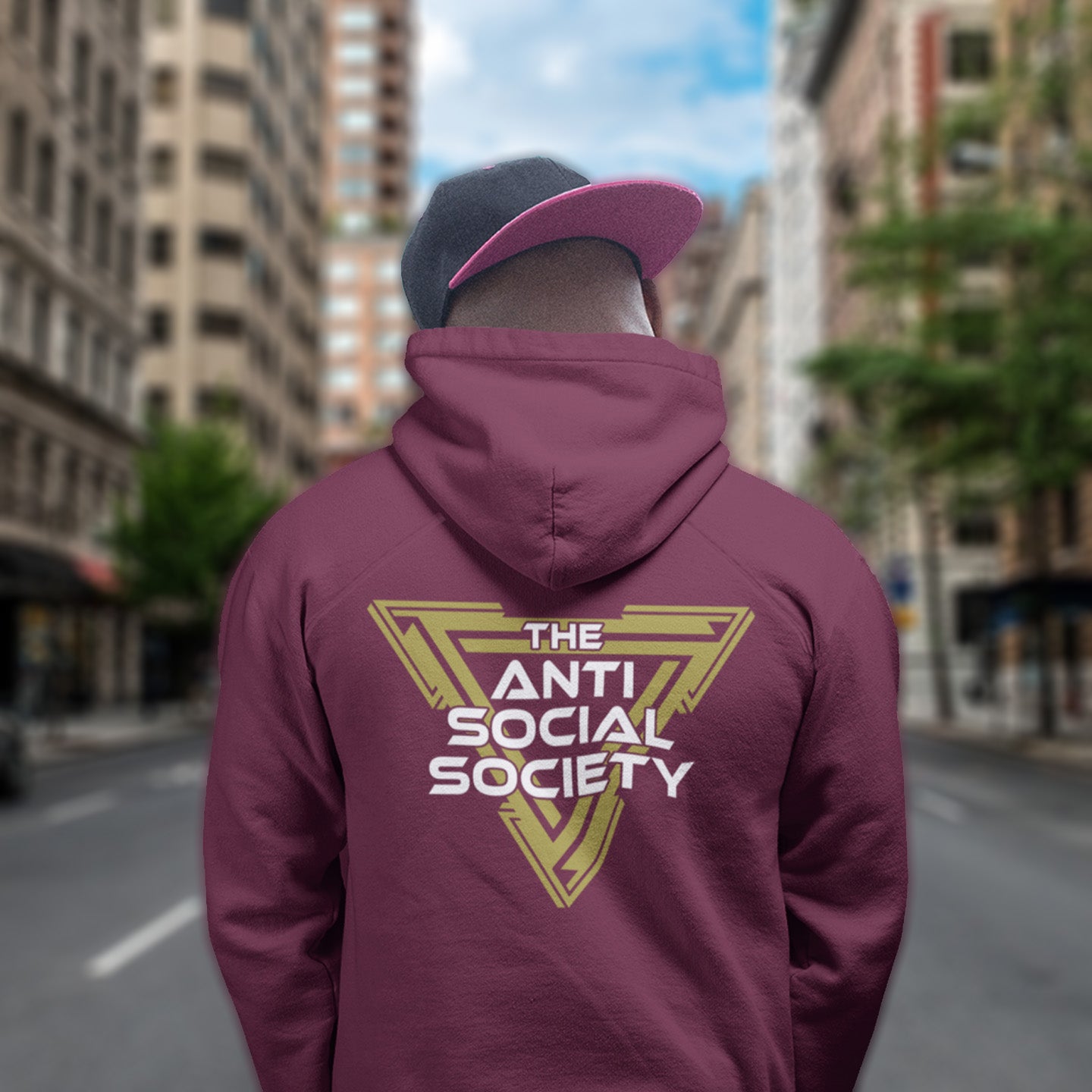 Person wearing a burgundy hoodie with 'The Anti Social Society' logo on the back, standing on a city street. This anti-social hoodie design gives you an oxymoron to ponder, the more and more you don't want to be a member, the more you become one. A satirical counterculture dig at modern society. Comfortable and practical. It's extra soft and has a convenient front pouch pocket. Made from organic cotton and recycled polyester, this social awareness hoodie is a great eco-friendly choice.