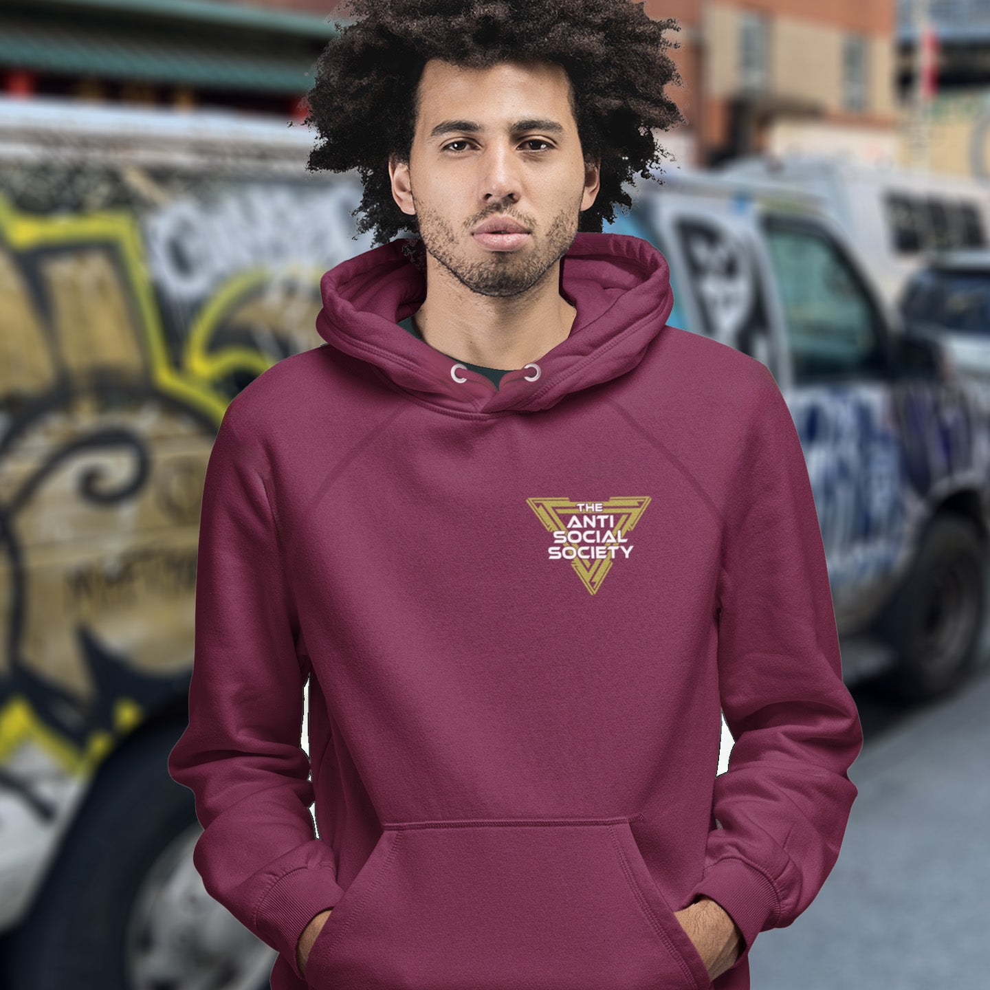 Man wearing a burgundy hoodie with a logo in an urban setting. This anti-social hoodie design gives you an oxymoron to ponder, the more and more you don't want to be a member, the more you become one. A satirical counterculture dig at modern society. Comfortable and practical. It's extra soft and has a convenient front pouch pocket. Made from organic cotton and recycled polyester, this social awareness hoodie is a great eco-friendly choice.