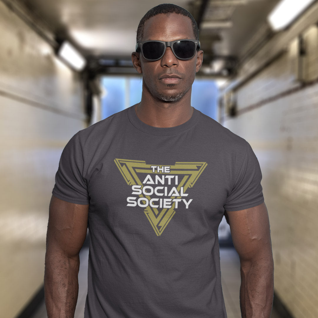 A man wearing an anthracite grey t-shirt with a yellow and white graphic that reads 'THE ANTI SOCIAL SOCIETY' and black sunglasses, standing in a brightly lit hallway.