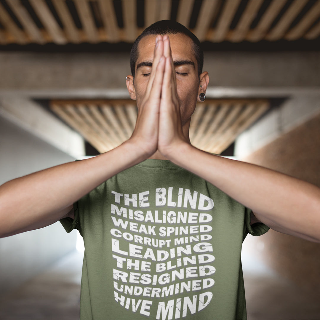 Person wearing a green t-shirt with text, standing with hands pressed together in front of face. An anti government t shirt suggesting that it's not just a case of the blind leading the blind anymore. It's now a lot more complicated. Show your social awareness of a dysfunctional society with this political slogan design. Made from 100% organic ring-spun cotton, this dystopian t shirt design is unisex, high-quality, super comfy, and best of all, eco-friendly.