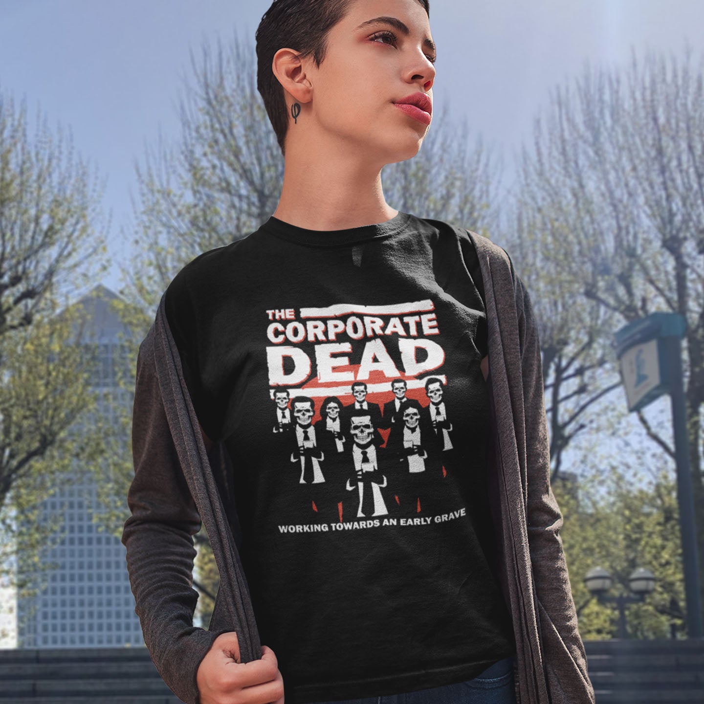 Person wearing a black t-shirt with 'The Corporate Dead' graphic design outdoors. A satirical t-shirt in an old horror movie design suggesting that working for a corporation is a soulless task. they can be faster and more efficient than a regular zombie, but dead inside nonetheless. Made from 100% organic ring-spun cotton, this satirical anti corporate t-shirt is unisex, high-quality, super comfy, and best of all, eco-friendly.