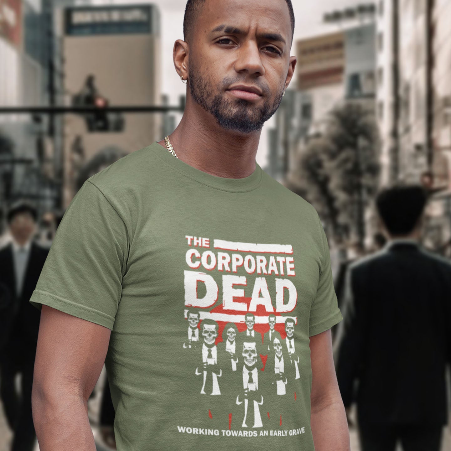 Man wearing a green t-shirt with 'The Corporate Dead' graphic design in an urban setting. A satirical t-shirt in an old horror movie design suggesting that working for a corporation is a soulless task. they can be faster and more efficient than a regular zombie, but dead inside nonetheless. Made from 100% organic ring-spun cotton, this satirical anti corporate t-shirt is unisex, high-quality, super comfy, and best of all, eco-friendly.