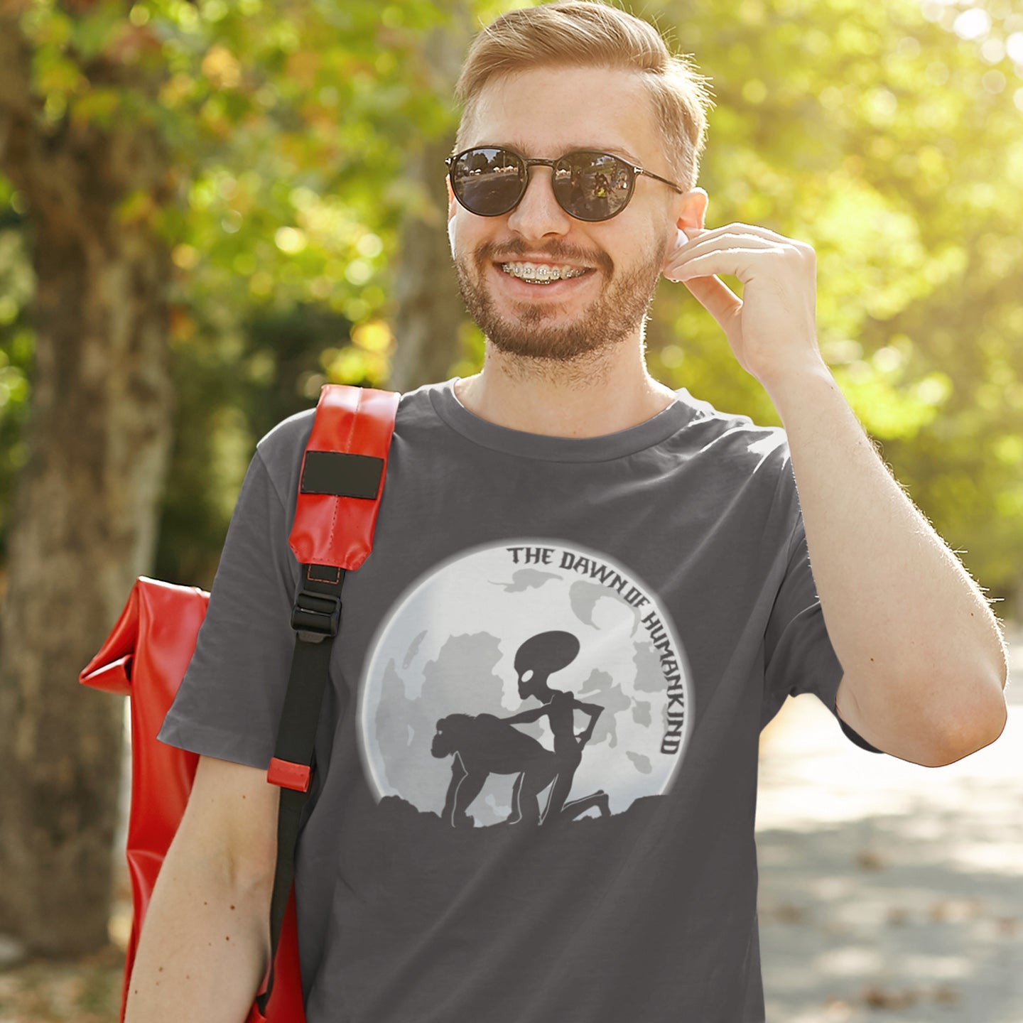 Man wearing sunglasses and a t-shirt with a graphic design outdoors. A hilarious alien conspiracy theory t-shirt depicting an one alternative reason for the evolution of humankind on this planet. One of many possibilities as to our origins and why there is such a great distance between us and the rest of the animal kingdom. Made from 100% organic ring-spun cotton, this conspiracy theory t-shirt is unisex, high-quality, super comfy, and best of all, eco-friendly.