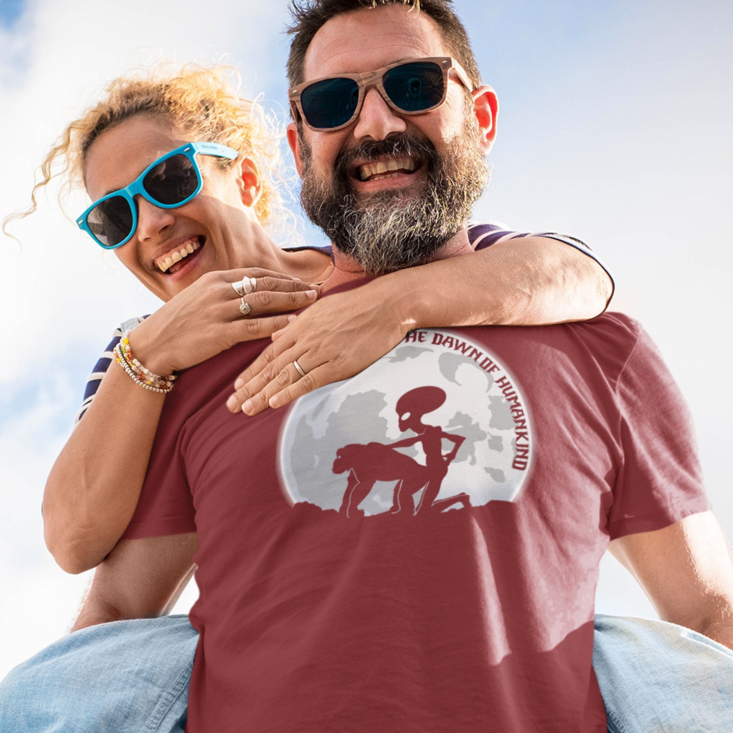 Man and woman hugging outdoors, man wearing a burgundy t-shirt with graphic design. A hilarious alien conspiracy theory t-shirt depicting an one alternative reason for the evolution of humankind on this planet. One of many possibilities as to our origins and why there is such a great distance between us and the rest of the animal kingdom. Made from 100% organic ring-spun cotton, this conspiracy theory t-shirt is unisex, high-quality, super comfy, and best of all, eco-friendly.