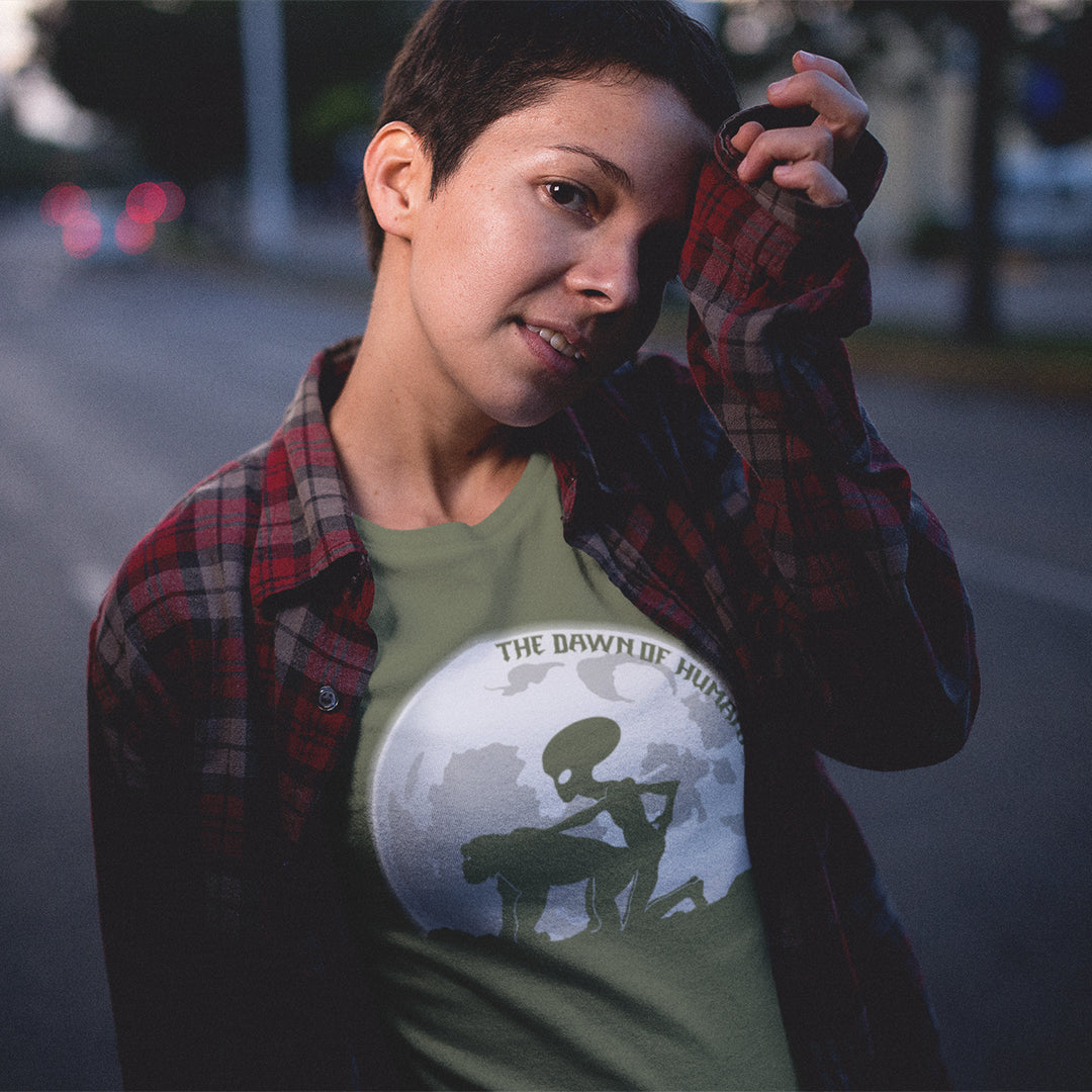 Woman standing in the street in a khaki alien t shirt. A hilarious alien conspiracy theory t shirt depicting an one alternative reason for the evolution of humankind on this planet. One of many possibilities as to our origins and why there is such a great distance between us and the rest of the animal kingdom. Made from 100% organic ring-spun cotton, this conspiracy theory t shirt is unisex, high-quality, super comfy, and best of all, eco-friendly.