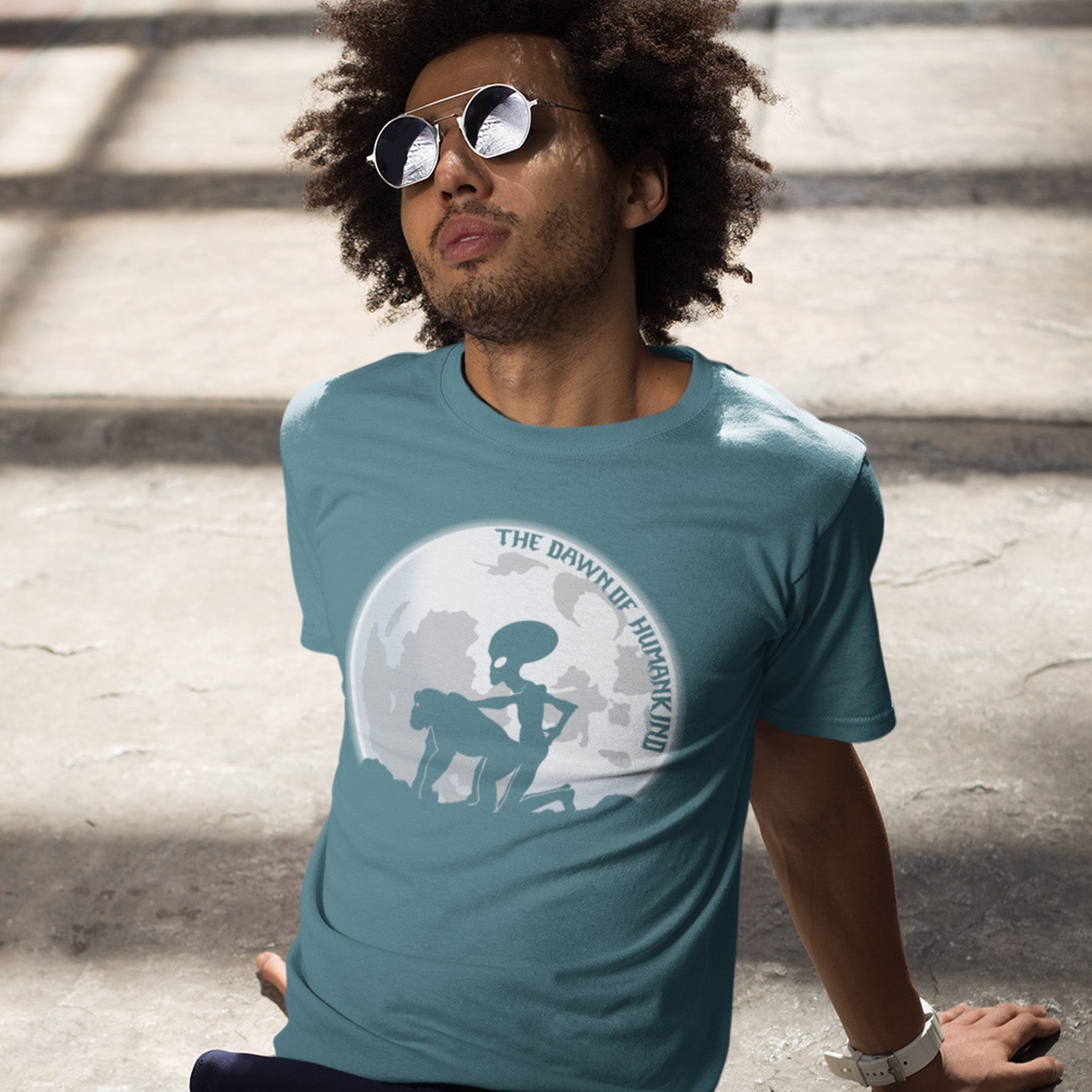 Man wearing a stargazer t-shirt with a graphic design, sitting on steps. A hilarious alien conspiracy theory t-shirt depicting an one alternative reason for the evolution of humankind on this planet. One of many possibilities as to our origins and why there is such a great distance between us and the rest of the animal kingdom. Made from 100% organic ring-spun cotton, this conspiracy theory t-shirt is unisex, high-quality, super comfy, and best of all, eco-friendly.