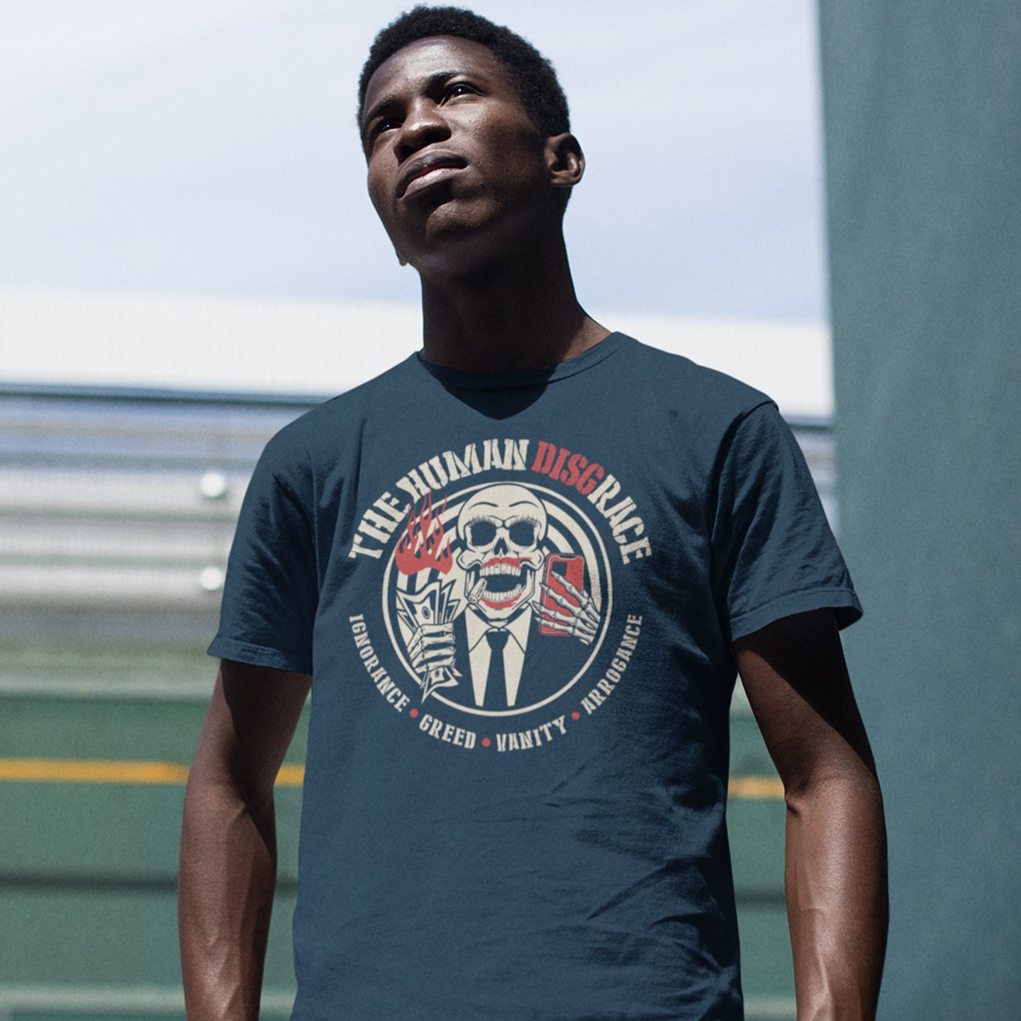 Man wearing a dark blue t-shirt with a graphic design outdoors. This broken society t shirt exposes the dark side of people. A great urban art design if you believe the human race has descended into a disgrace and we need educating about our own weaknesses before it's too late. Made from 100% organic ring-spun cotton, these social issues t shirts are unisex, high quality, super comfy, and best of all, eco-friendly.