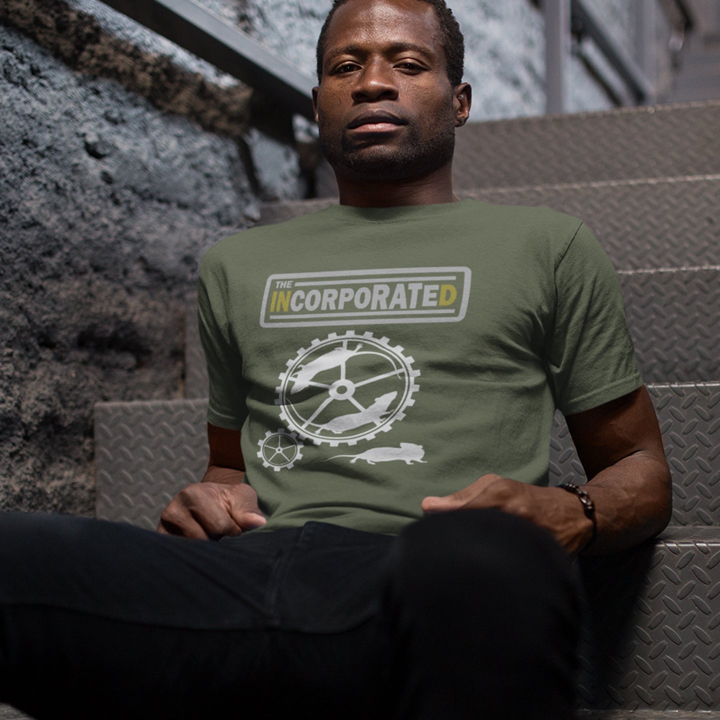 Man wearing a khaki t-shirt with a logo sitting on steps. This non conformist t shirt questions the effects of a corporate run society. Have we just created a corporate cult to follow ? A satirical and alternative view of the modern rat race. Made from 100% organic ring-spun cotton, this counter culture t shirt is unisex, high-quality, super comfy, and best of all, eco-friendly.