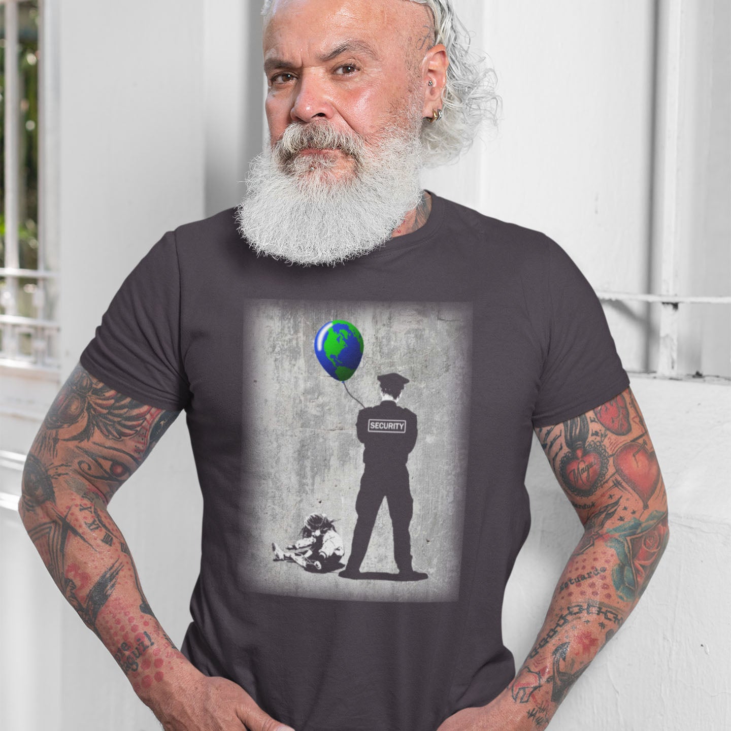 Man wearing a t-shirt with a graphic design of a security guard and a child with a balloon shaped like the Earth. A Banksy style graffiti t-shirt with a political message suggesting that we possible left the world in the wrong hands while being distracted. Save the planet by giving it back to the children. Made from 100% organic ring-spun cotton, this graffiti stencil art t-shirt is unisex, high-quality, super comfy, and best of all, eco-friendly.