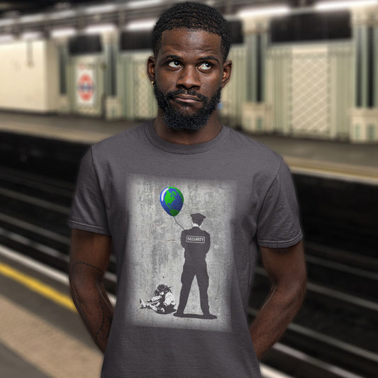 A man wearing a dark gray graphic t-shirt in a subway station. The t-shirt features a parody print of Banksy's 'Girl with a Pink Balloon' style, showing a security guard silhouette holding a blue and green globe balloon, with the word 'SECURITY' on the back.