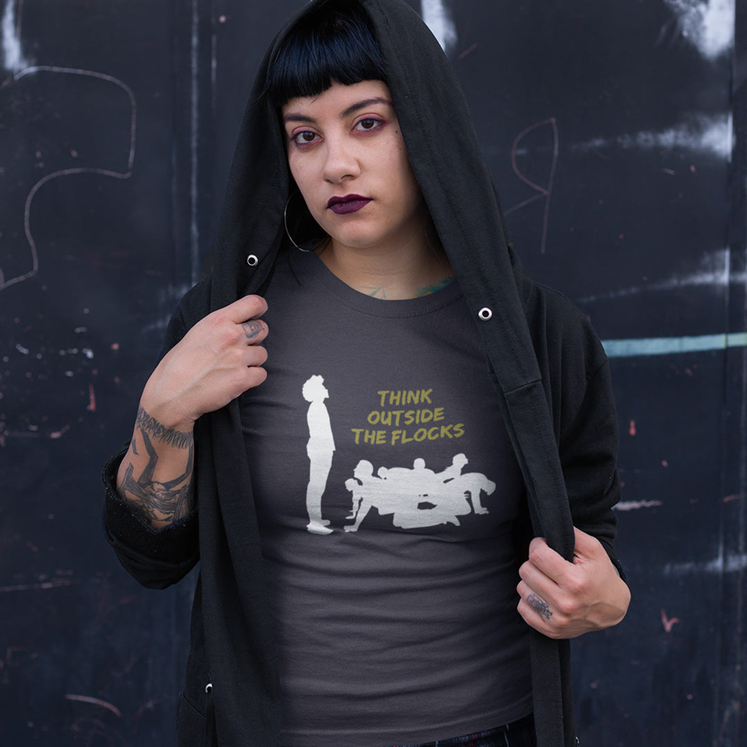 A person wearing a dark charcoal gray t-shirt with a white graphic and yellow text reading 'THINK OUTSIDE THE FLOCKS', layered under a black hoodie, standing against a dark graffiti wall.